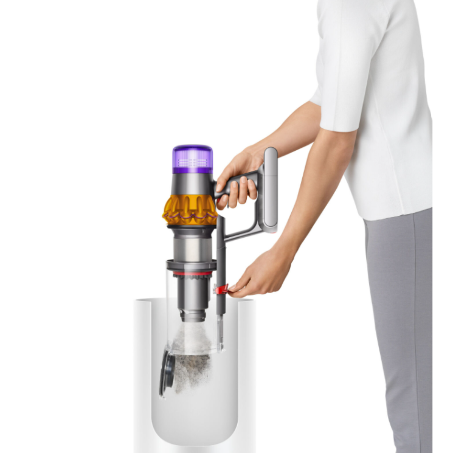 Une personne tient un aspirateur Dyson au-dessus d'un récipient transparent, levier rouge activé.