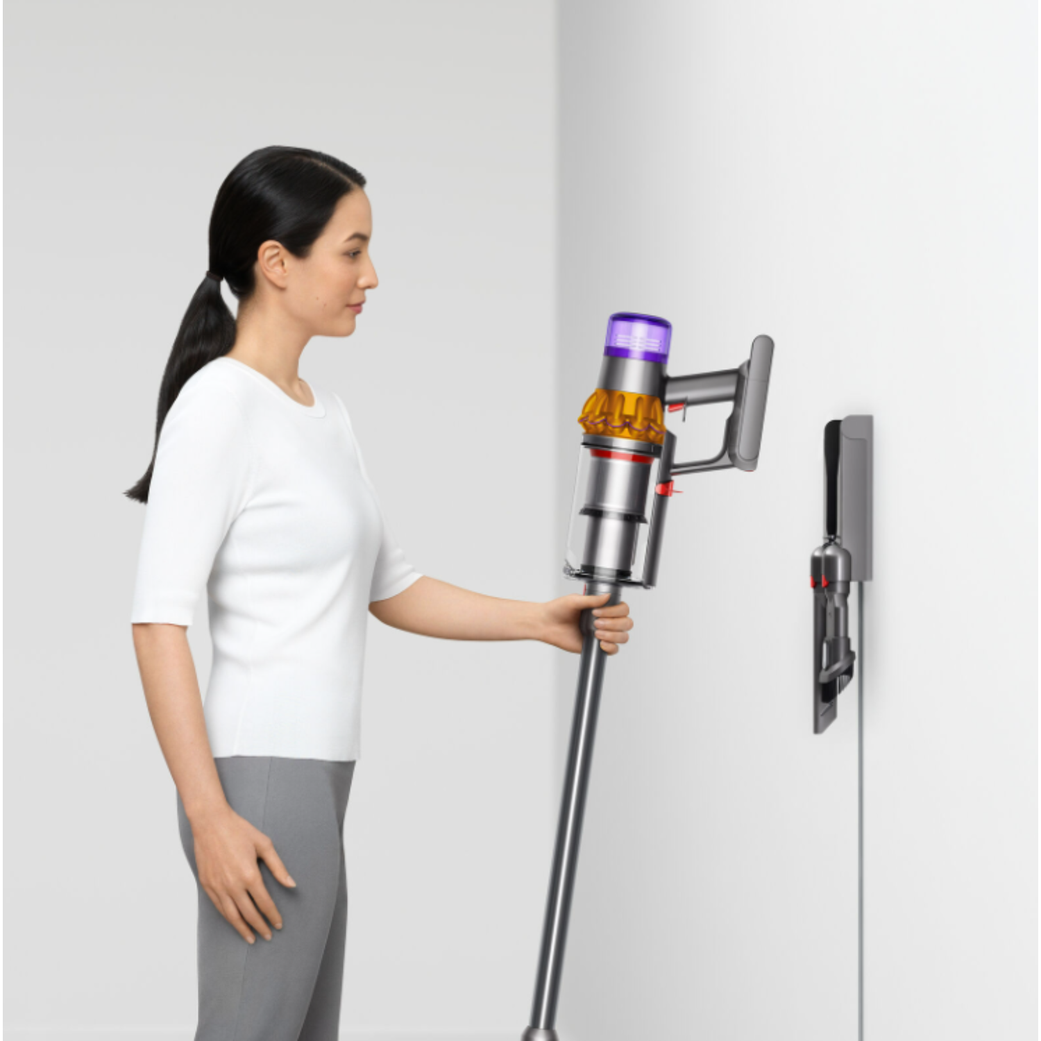 Femme tenant un aspirateur sans fil à côté d'une station de charge murale.