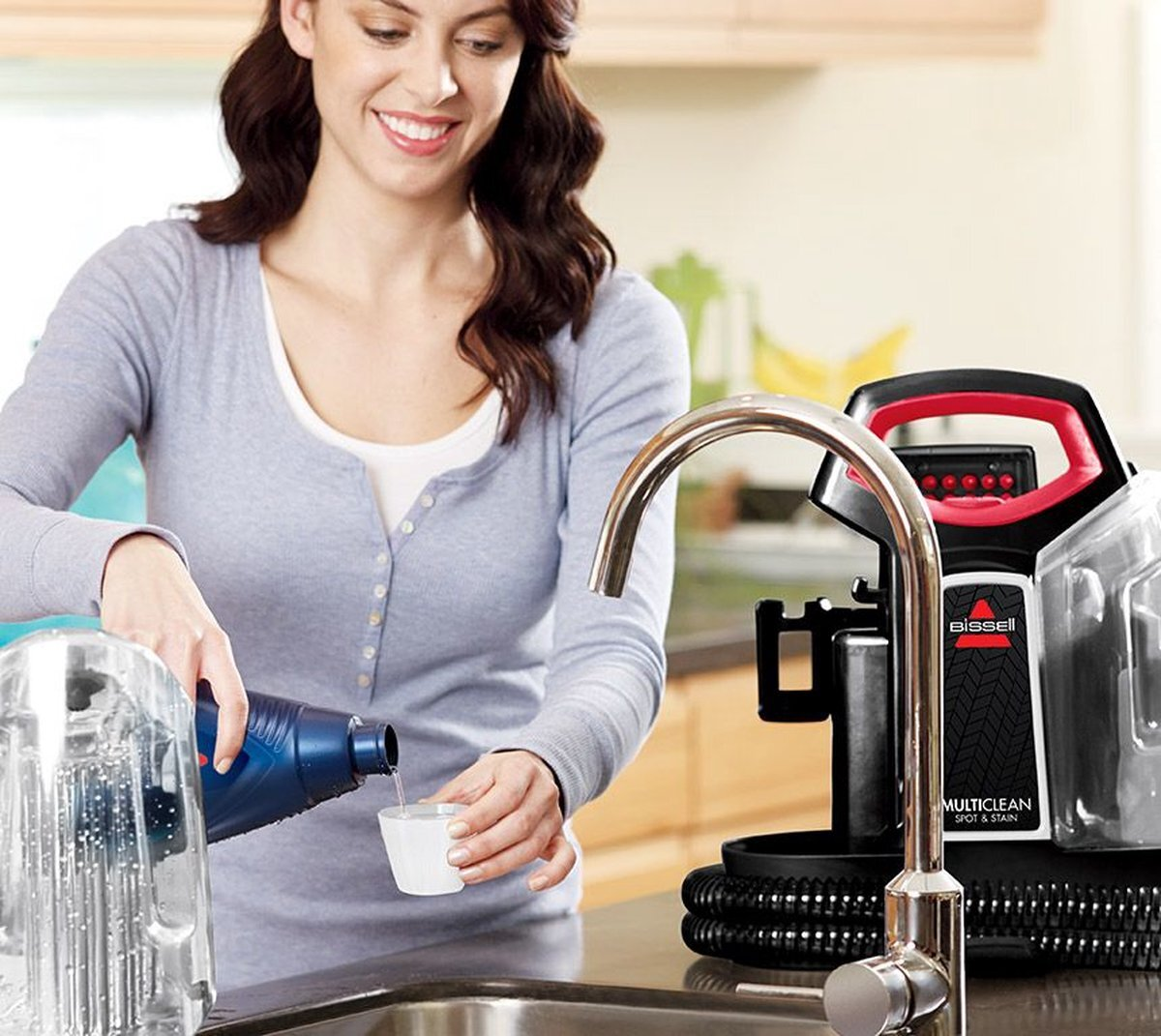 Kobieta wlewa płyn z niebieskiej butelki do miarki, w pobliżu zlewu i środka czyszczącego.