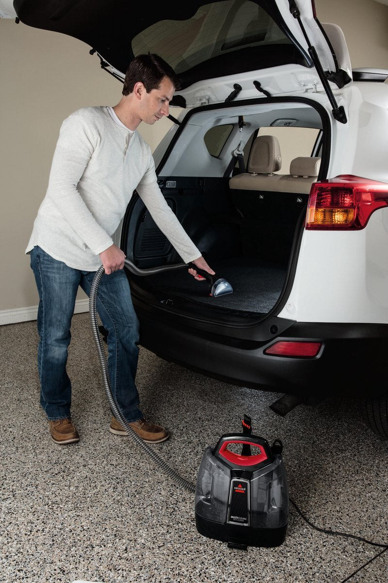 Mężczyzna odkurzający wnętrze białego samochodu. Odkurzacz Bissel na podłodze.