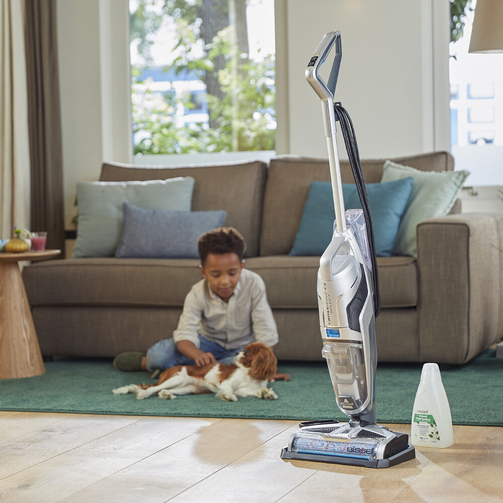 Chłopiec głaszcze psa, a obok stoi odkurzacz Bissell na zielonym dywanie.