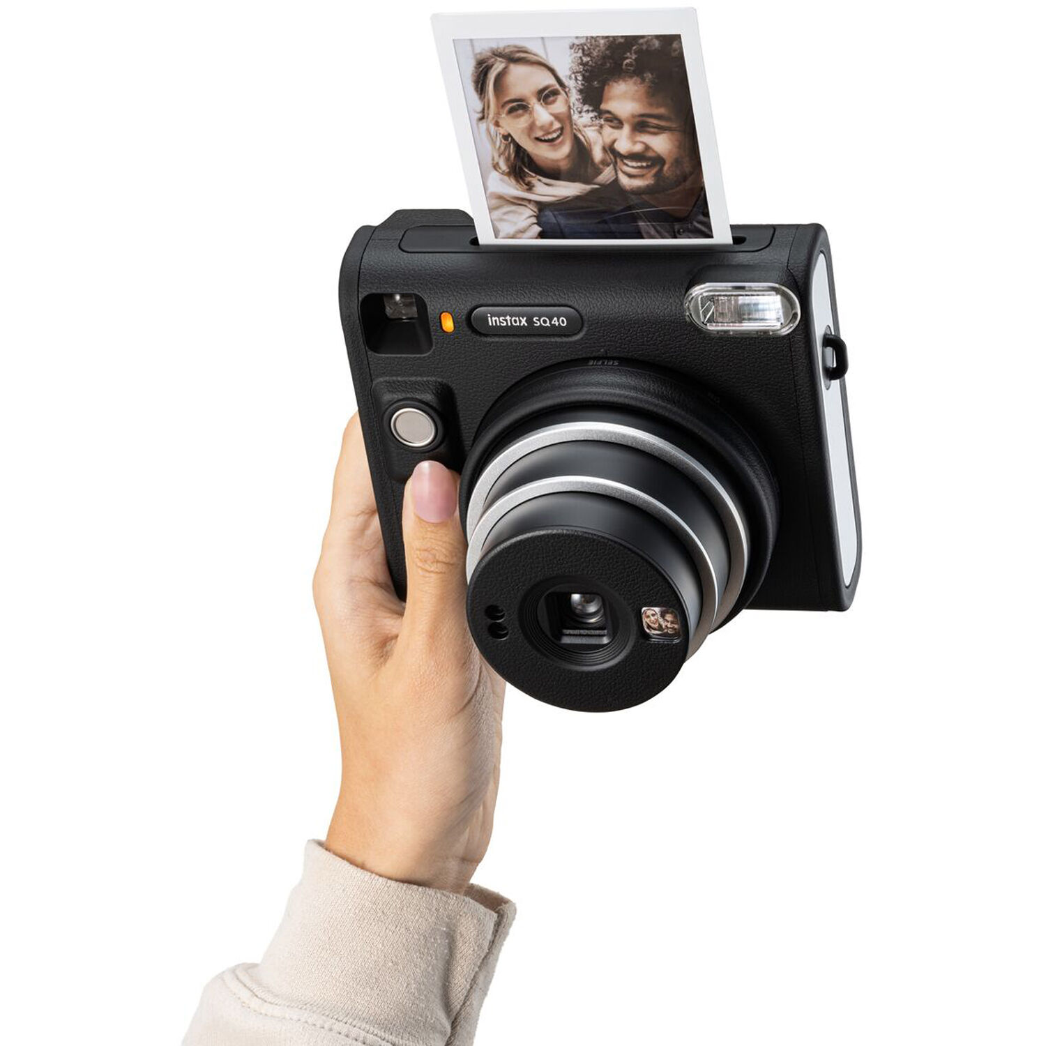 A person holds a black instant camera, and a printed photo is emerging from it.