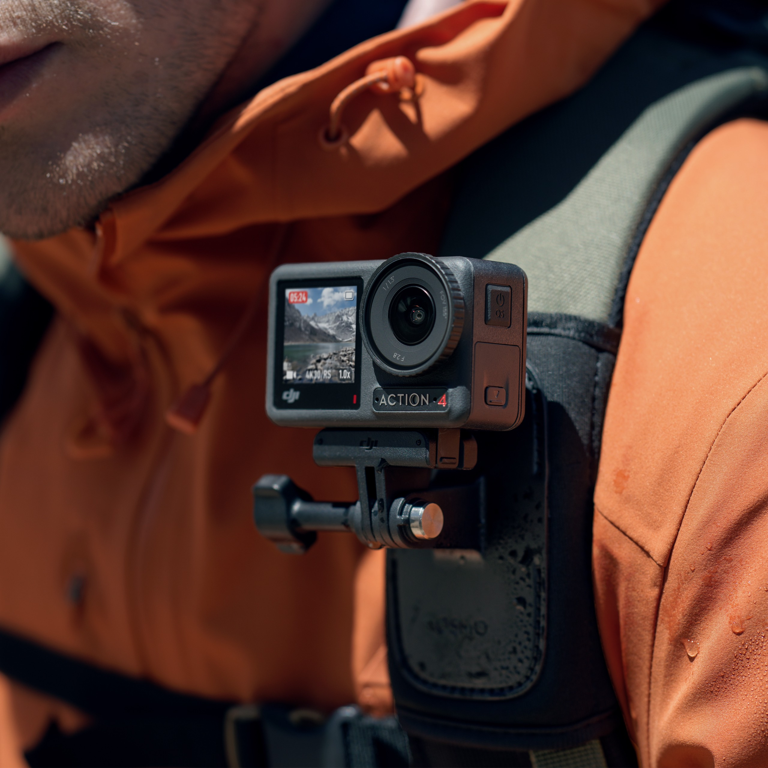 Eine schwarze Action-Kamera an einer Brusthalterung mit Person in orangefarbener Jacke.