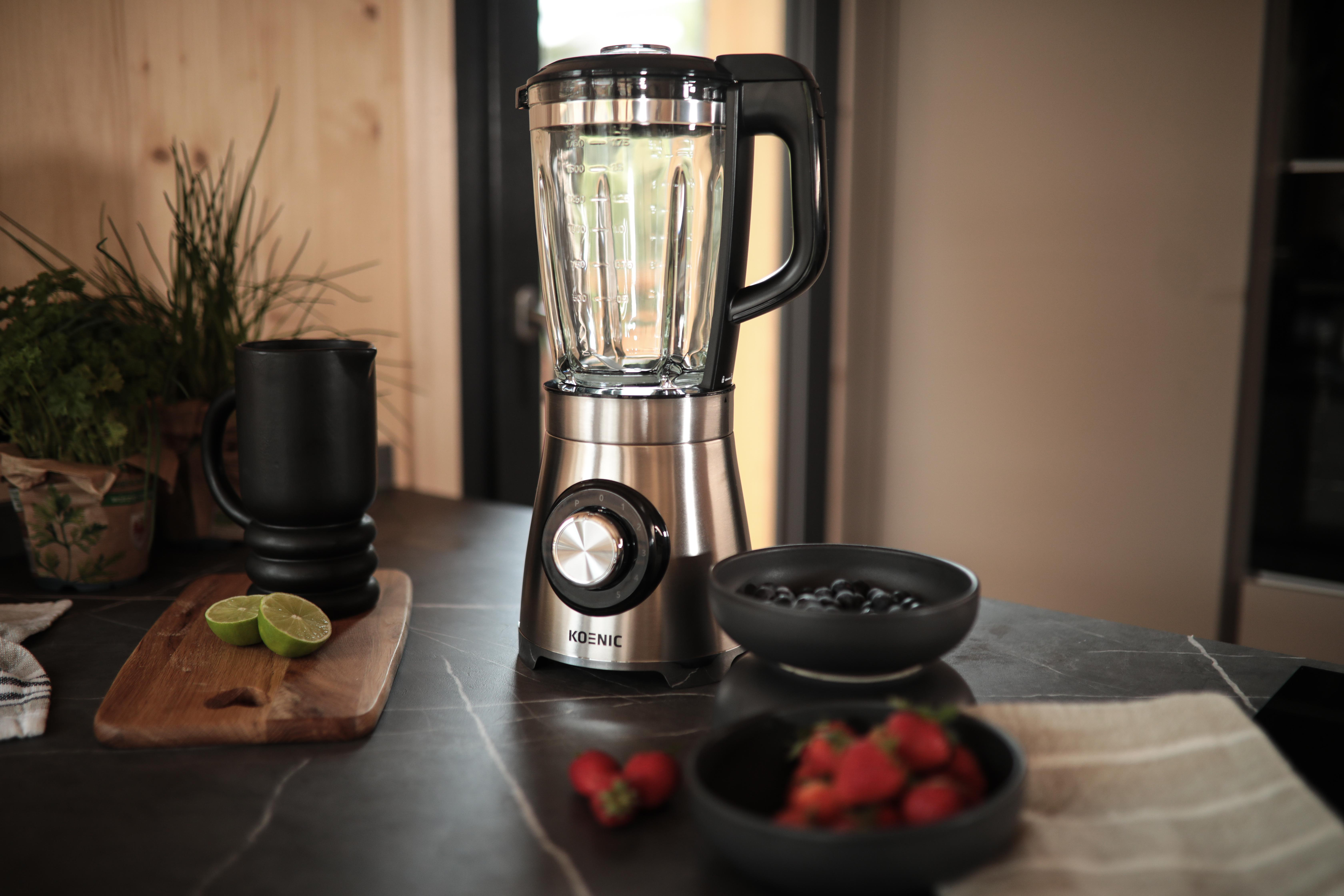 Mixer auf Marmortisch mit schwarzem Becher, Holzbrett und Obstschalen.