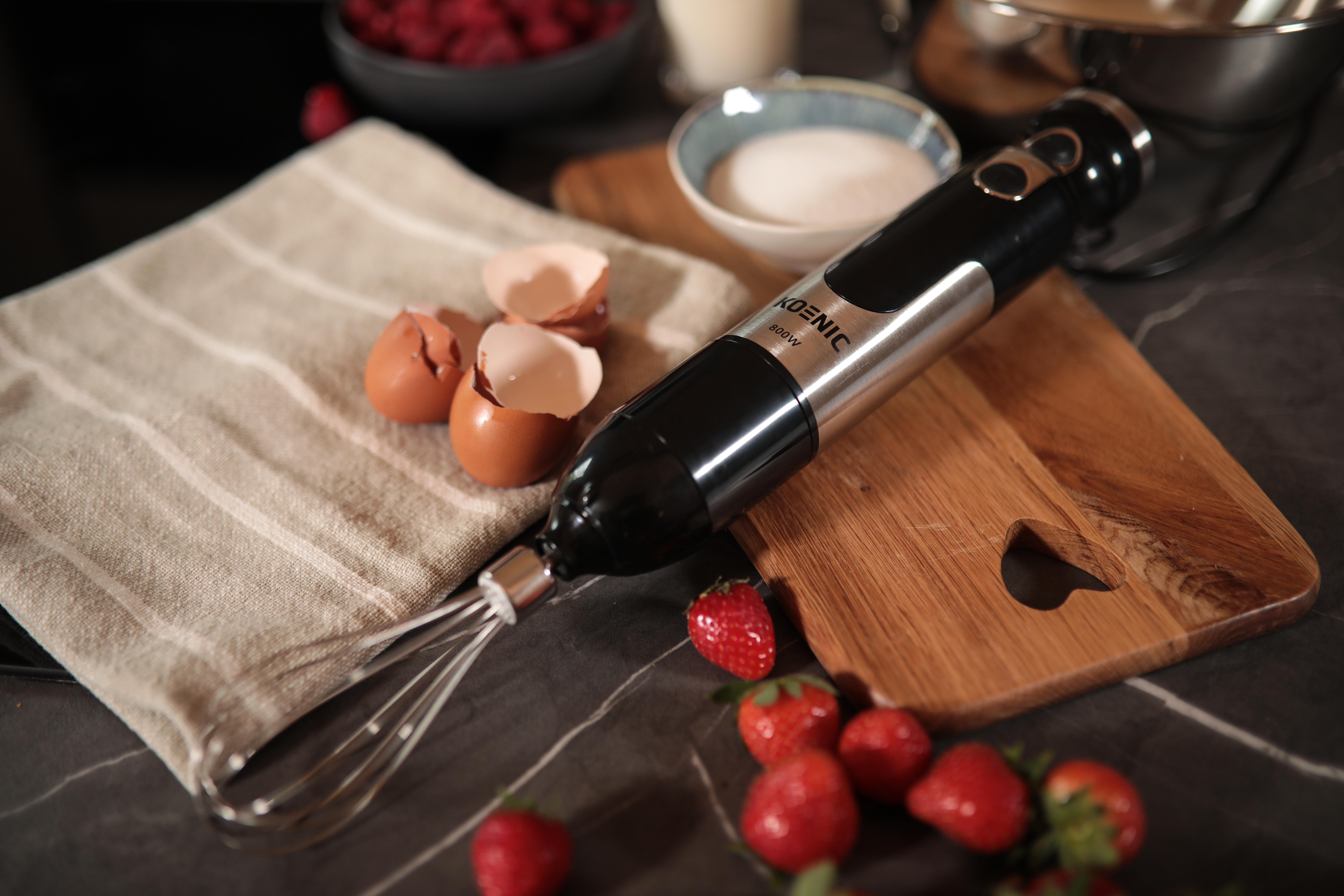 Handmixer auf Holzbrettern. Eier, Erdbeeren und Zutaten in der Nähe.