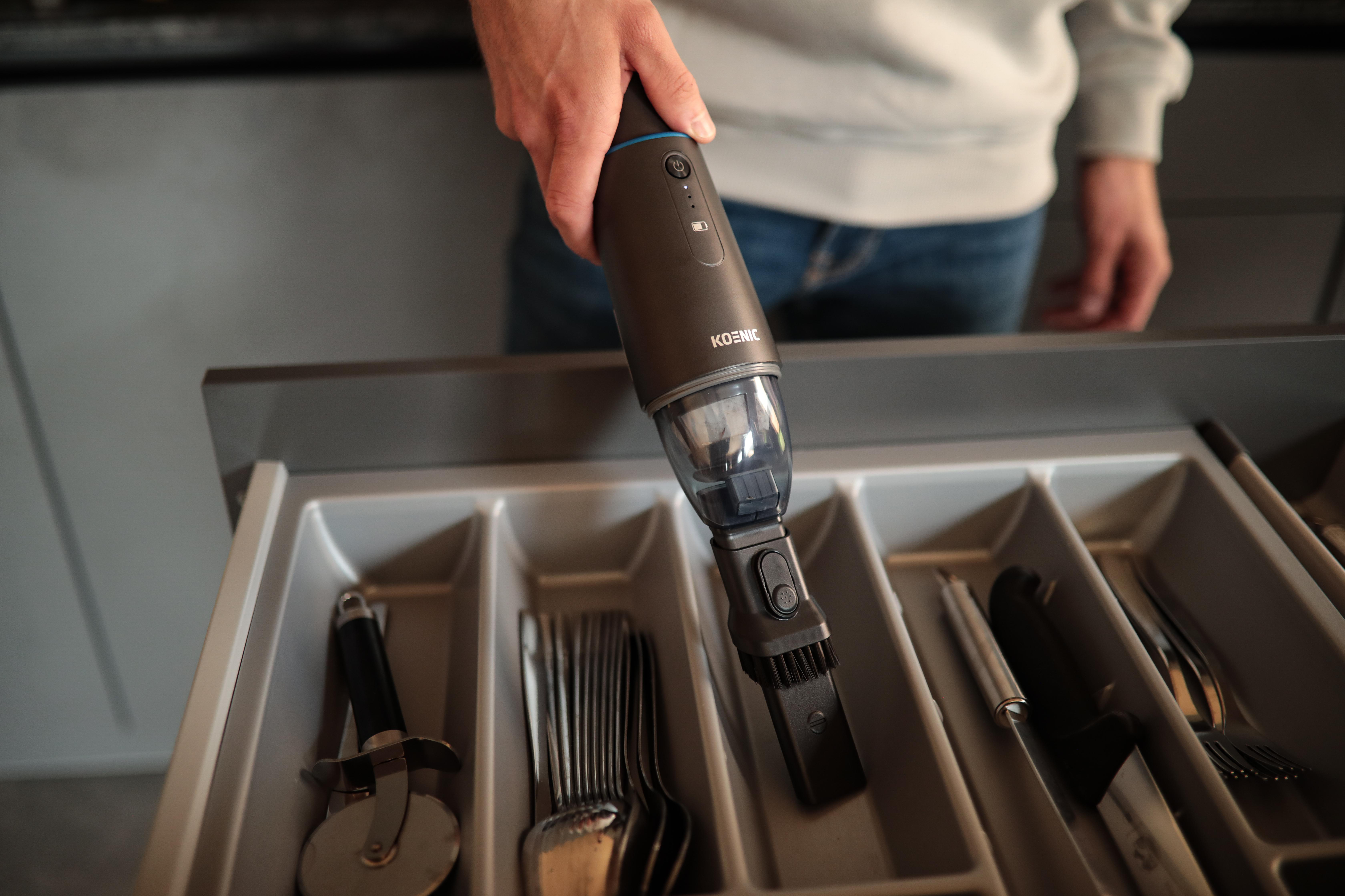 Hand legt schwarzen Staubsauger in Schublade mit Utensilien.