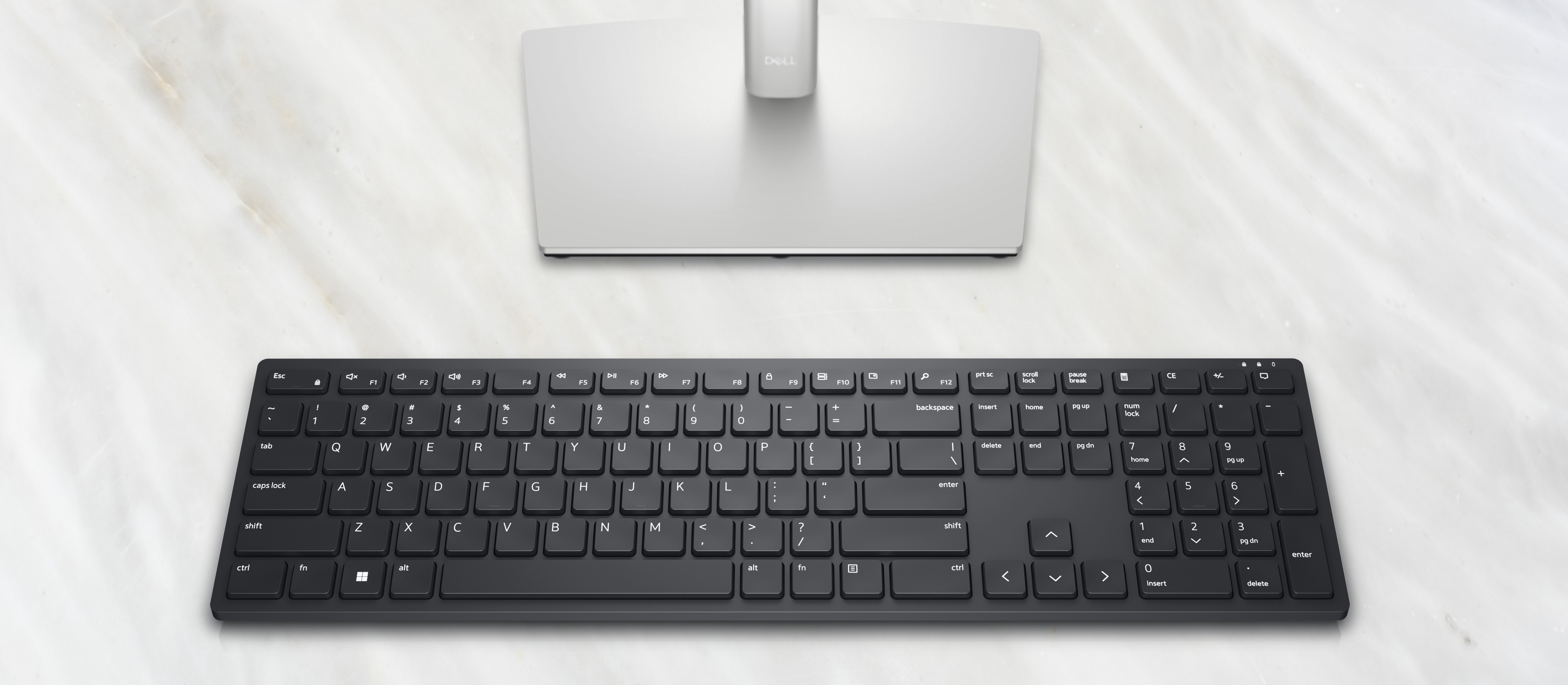 Schwarze Tastatur und Dell-Monitor auf weißer Marmoroberfläche. Die Tastatur ist zentriert.