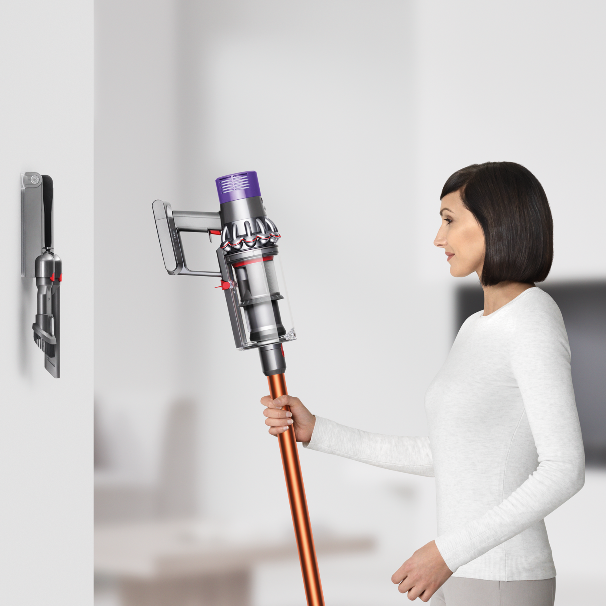 Frau hält einen Dyson-Staubsauger in der Nähe einer Wandhalterung.
