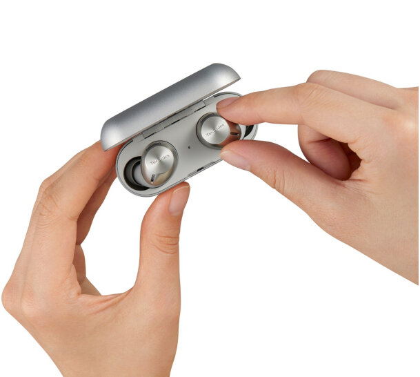 Dłonie trzymają białe etui ładujące ze słuchawkami w środku.