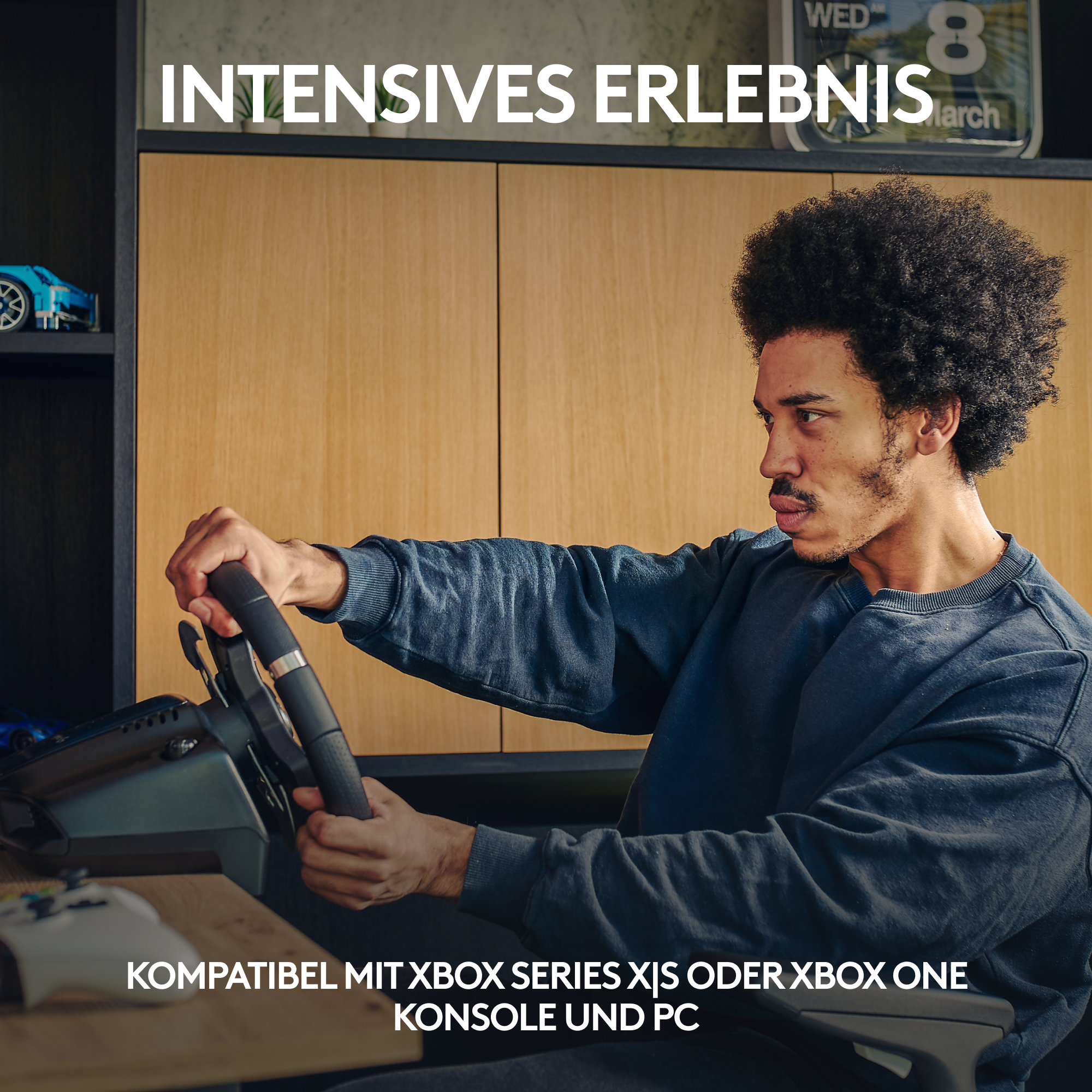 Ein Mann benutzt ein Rennlenkrad-Setup, Werbung für Spielkonsole sichtbar.