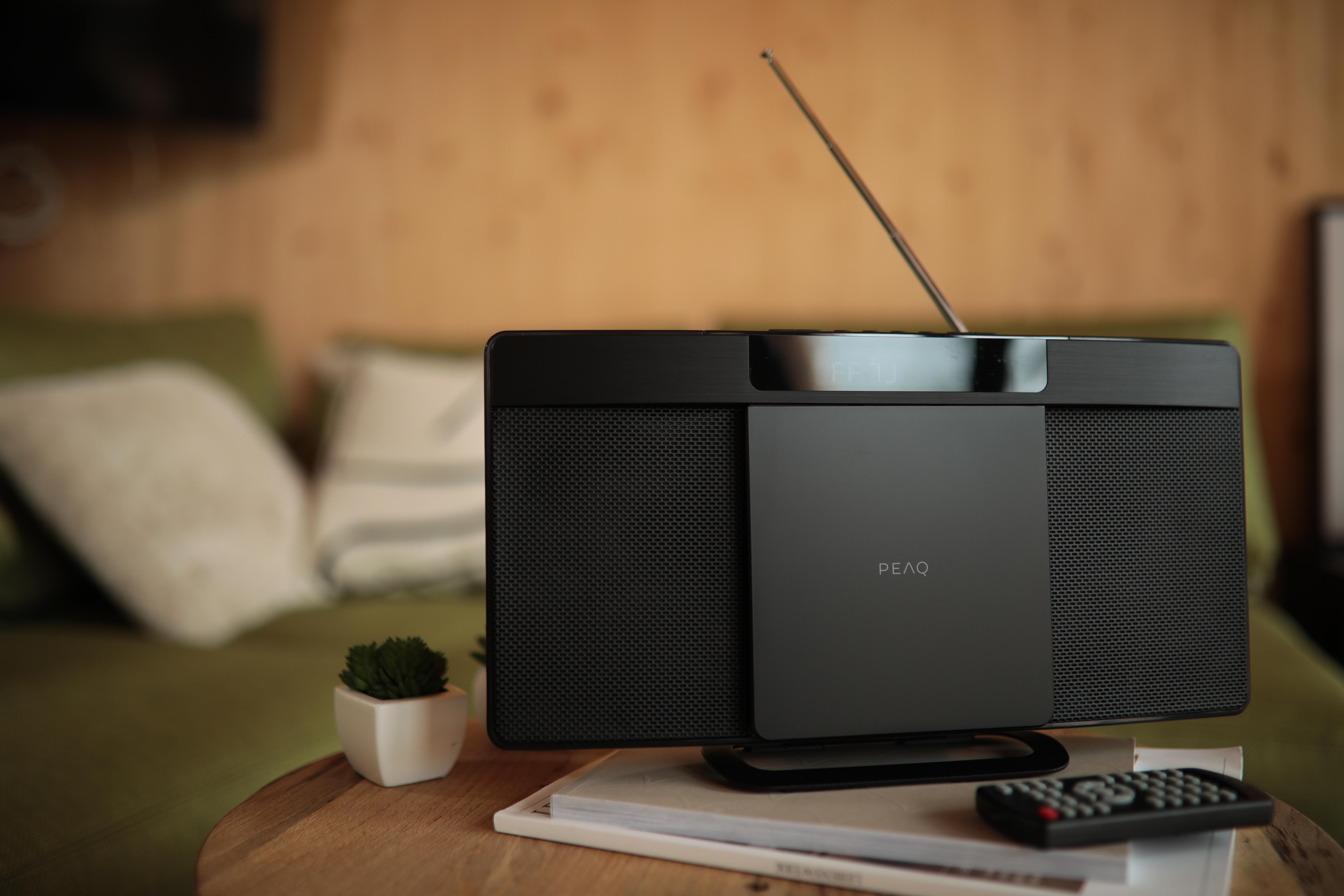 Schwarzes Radio mit Display, silberner Antenne und Fernbedienung. Auf einem Holztisch.