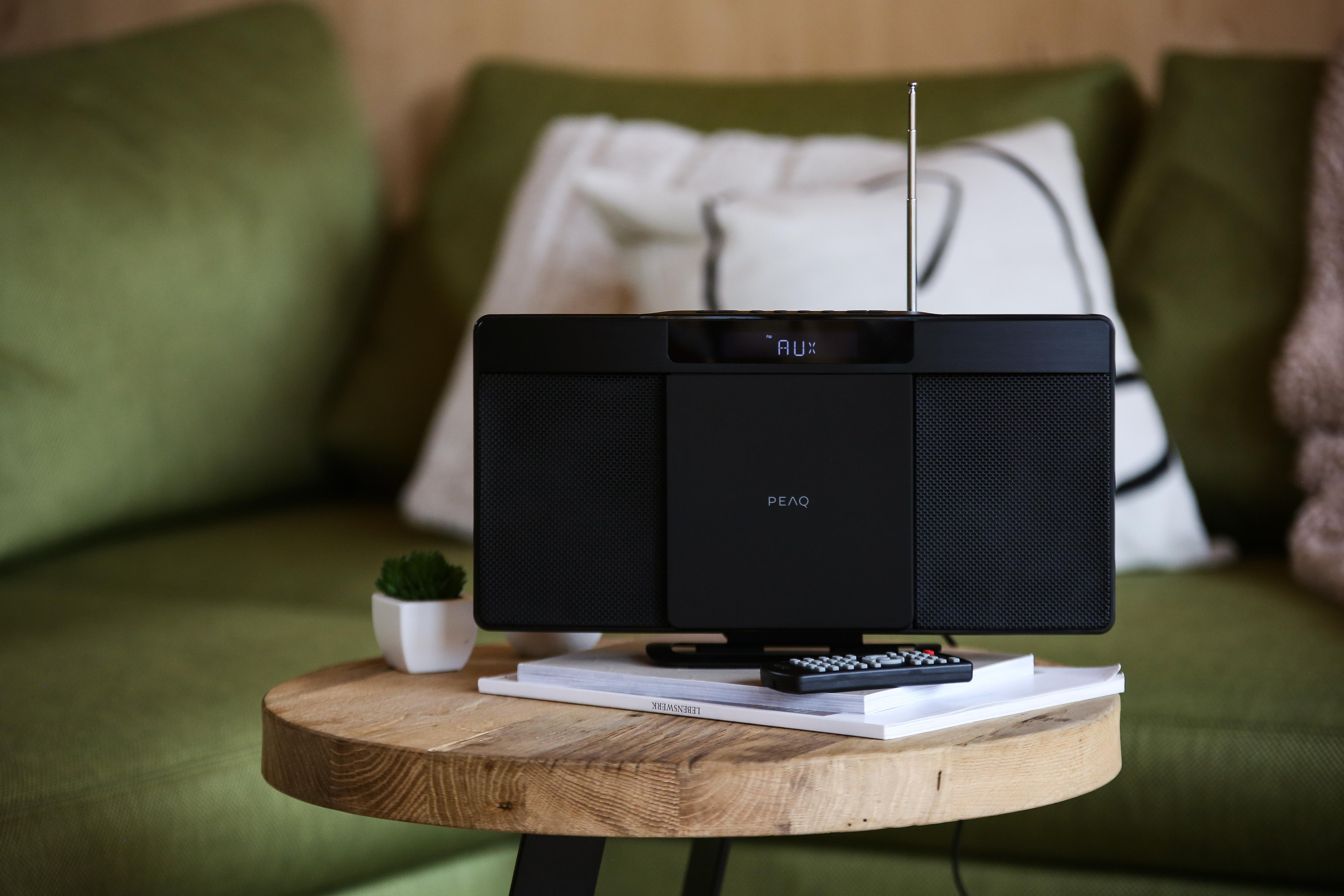 Schwarzes Soundsystem auf Holztisch, grünes Sofa im Hintergrund.