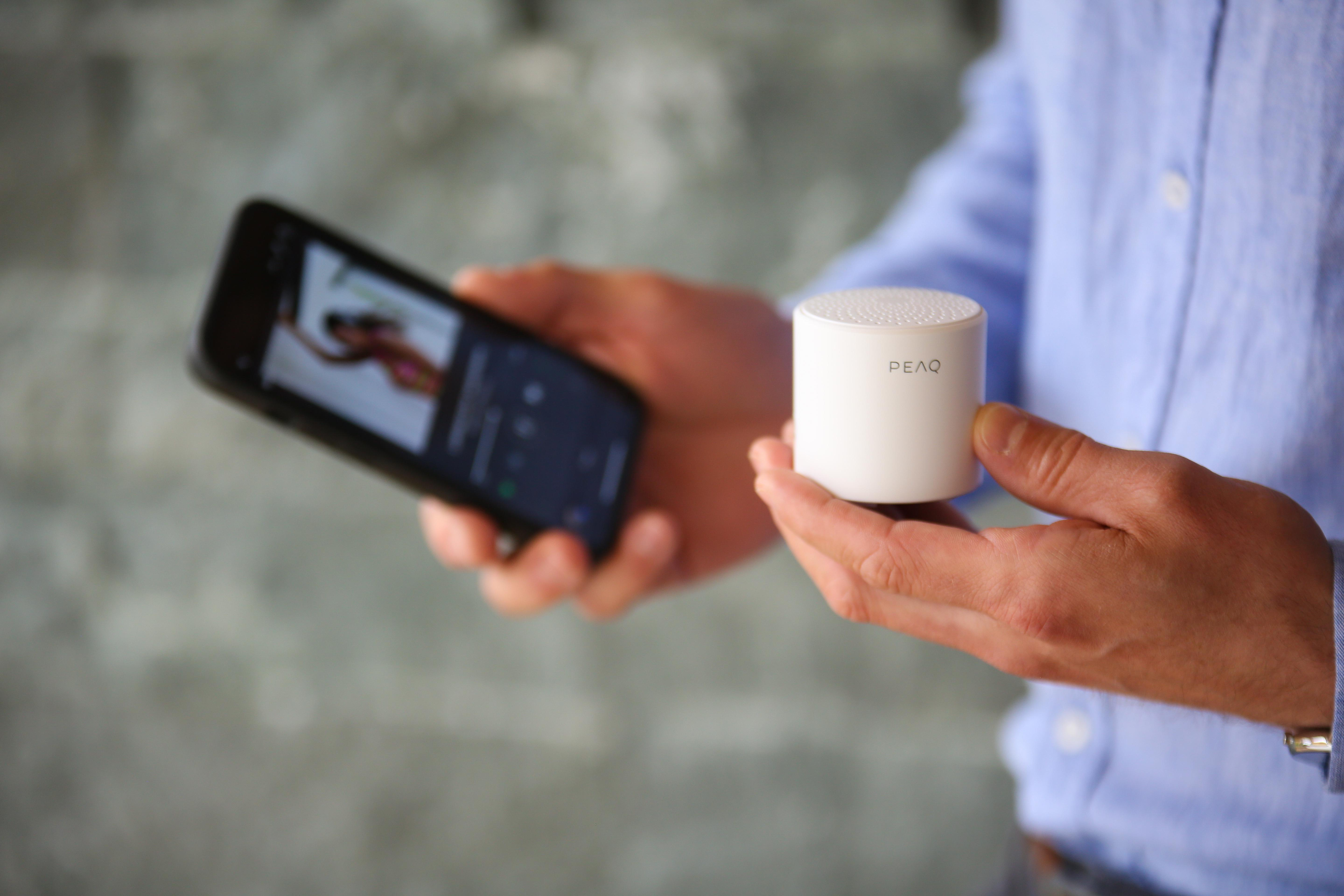 Person hält weißen Lautsprecher und Smartphone mit Musik-App.