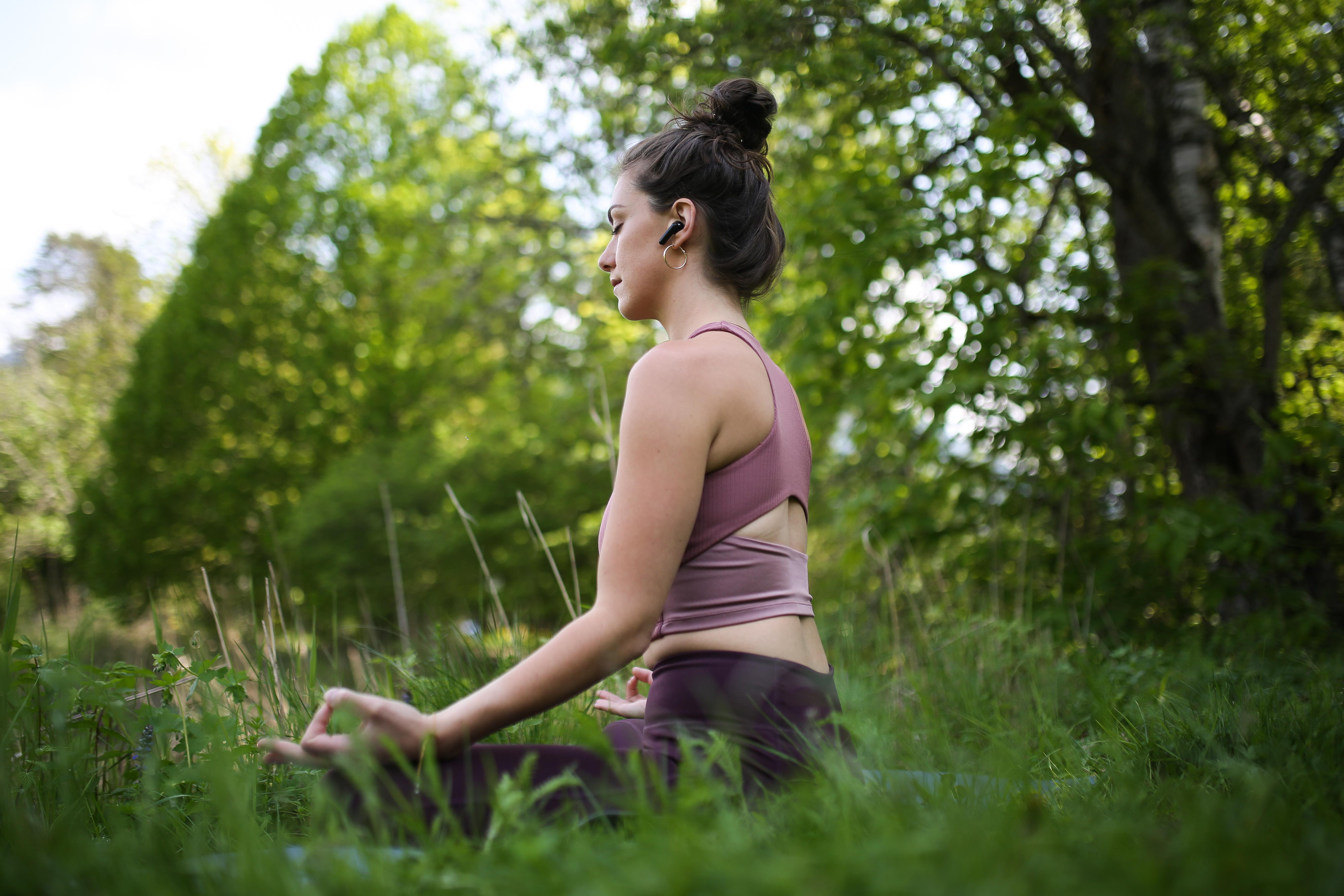 Frau in Yoga-Pose in einem grünen Feld, trägt Kopfhörer.