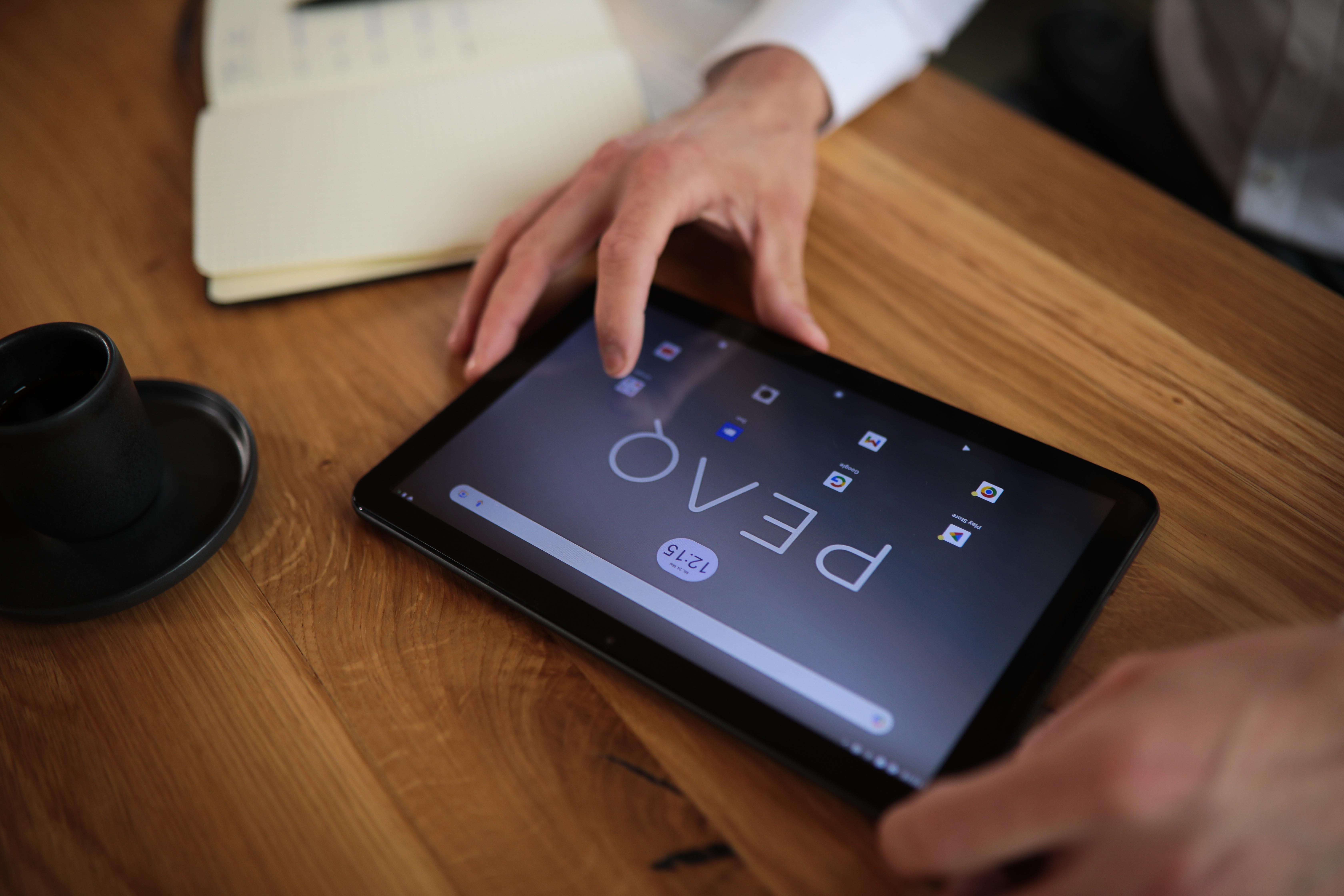 Die Hände einer Person liegen auf einem Tablet, der Bildschirm zeigt ein Logo.