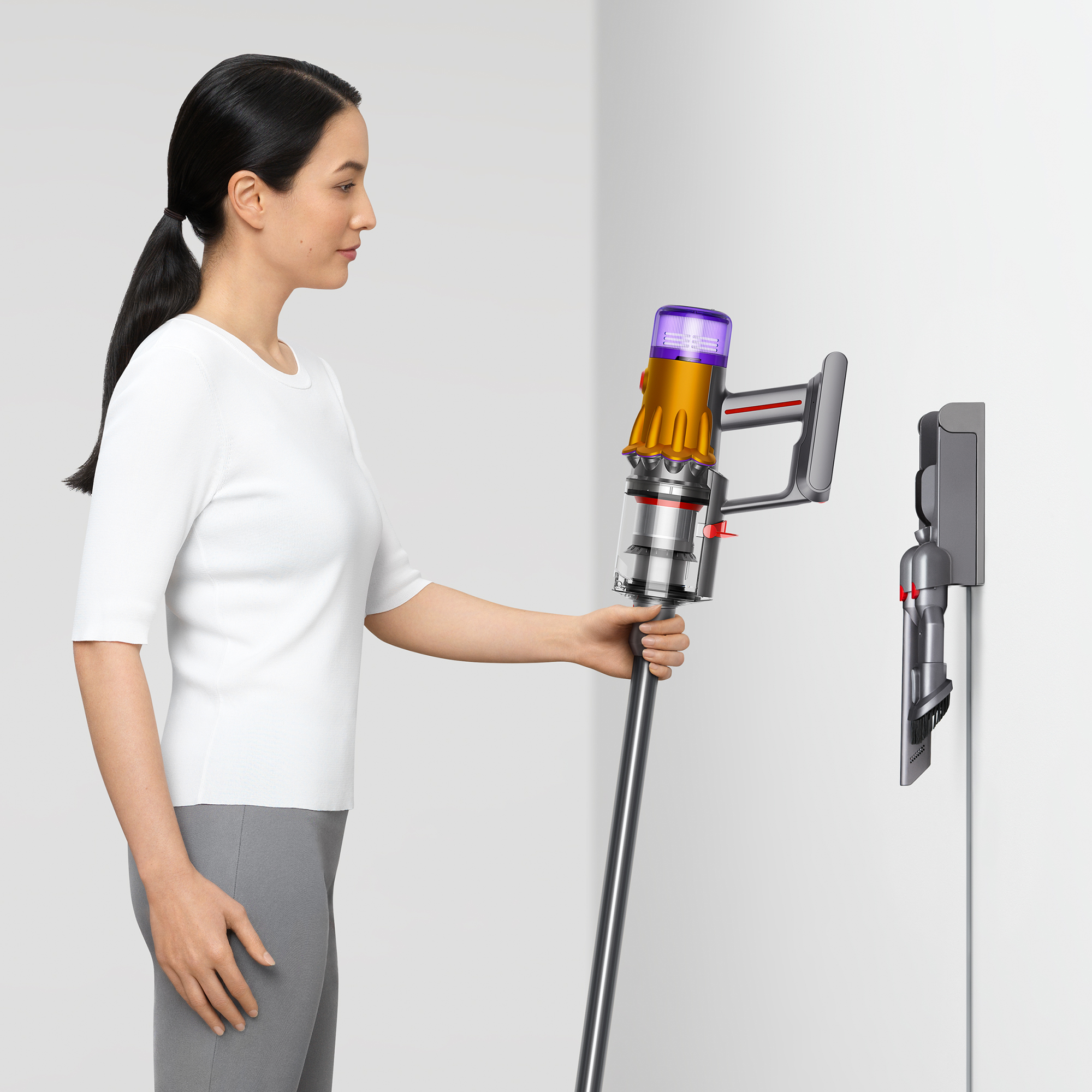 Frau hält einen Dyson-Staubsauger in der Nähe eines wandmontierten Ladegeräts.