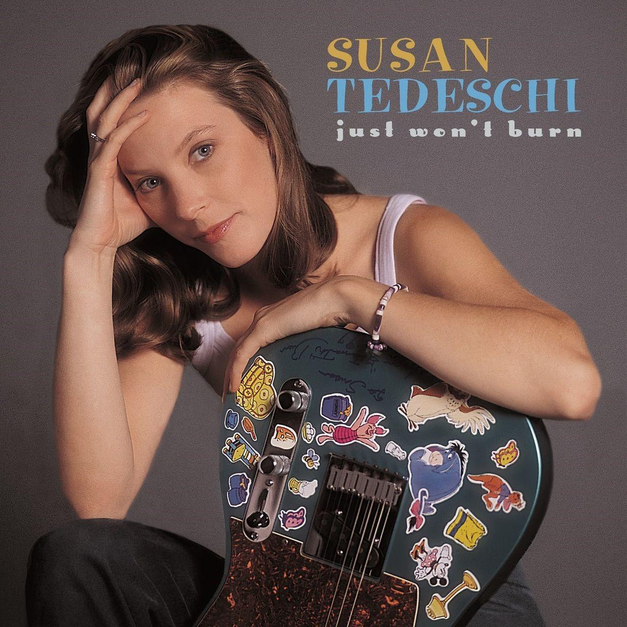 Albumcover: Frau mit Gitarre, hält sie. Aufkleber auf der Gitarre. Grauer Hintergrund.