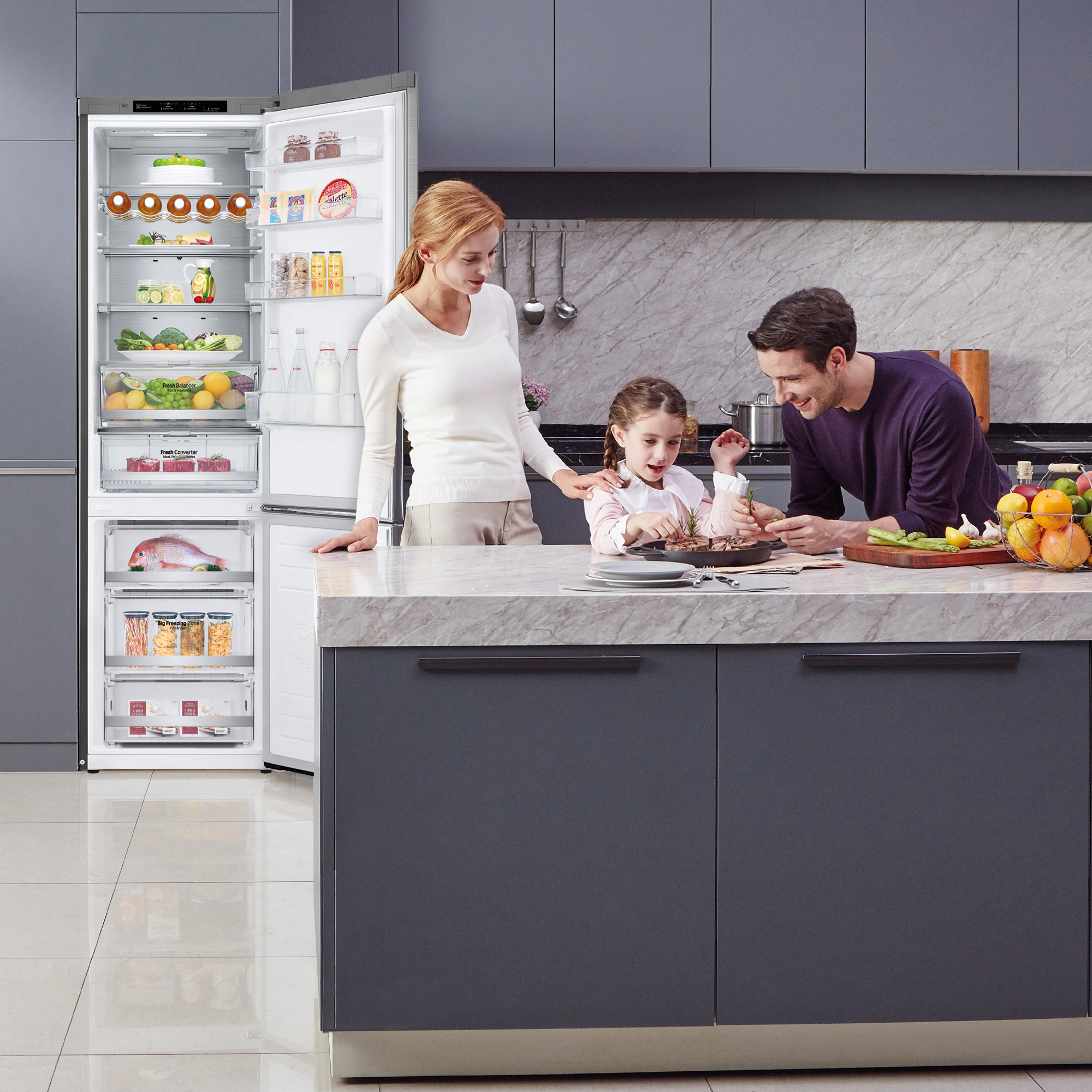 Familia en la cocina preparando comida, refrigerador abierto con comida. Encimera de mármol. Armarios grises.