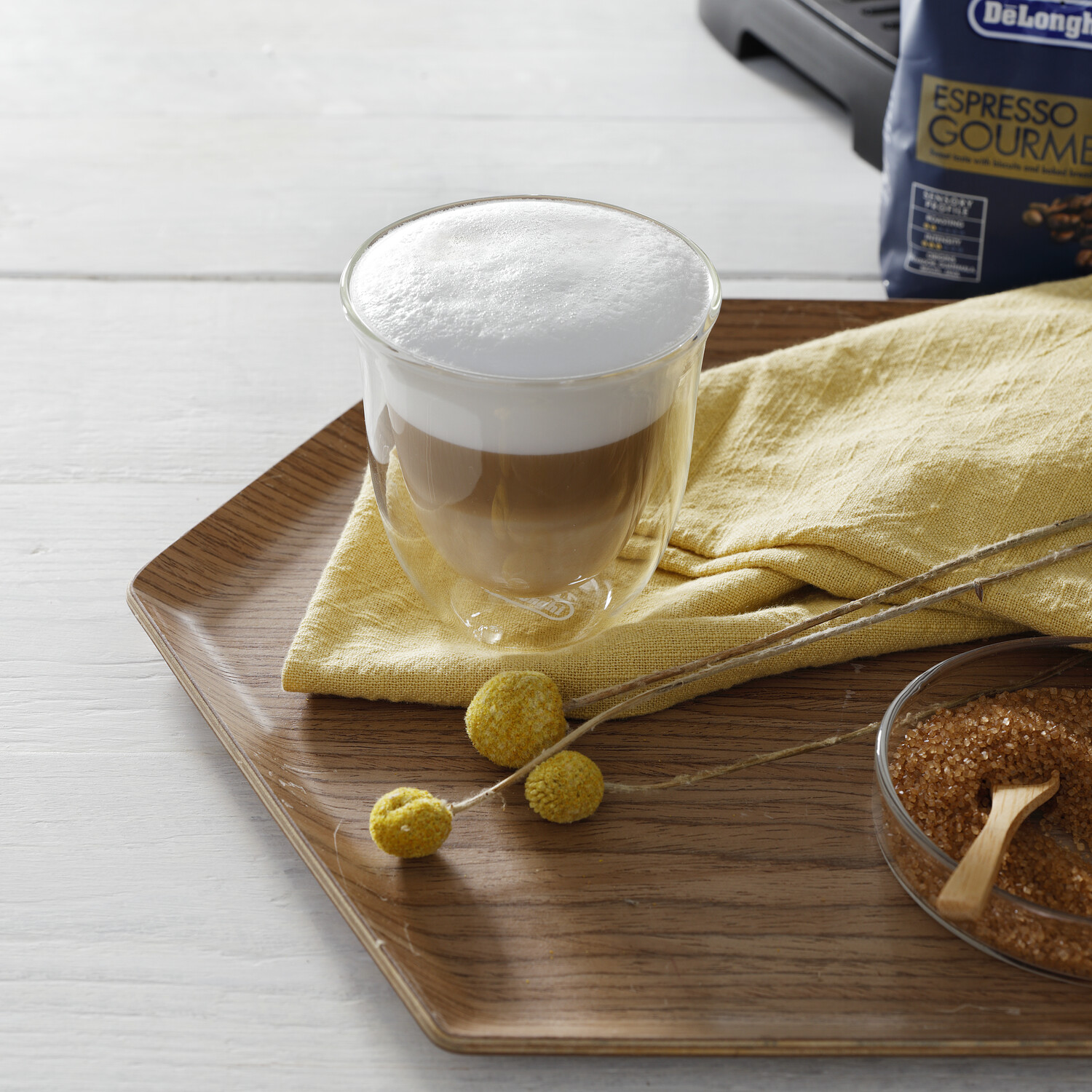Latte en un vaso de doble pared en una bandeja de madera, con azúcar y bolsa de granos de café.