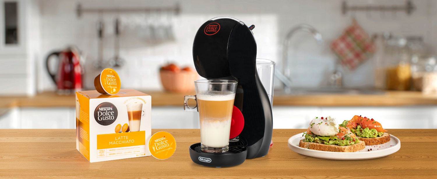 Cafetera, cápsulas de café, latte y comida en una mesa de madera. Fondo de cocina.