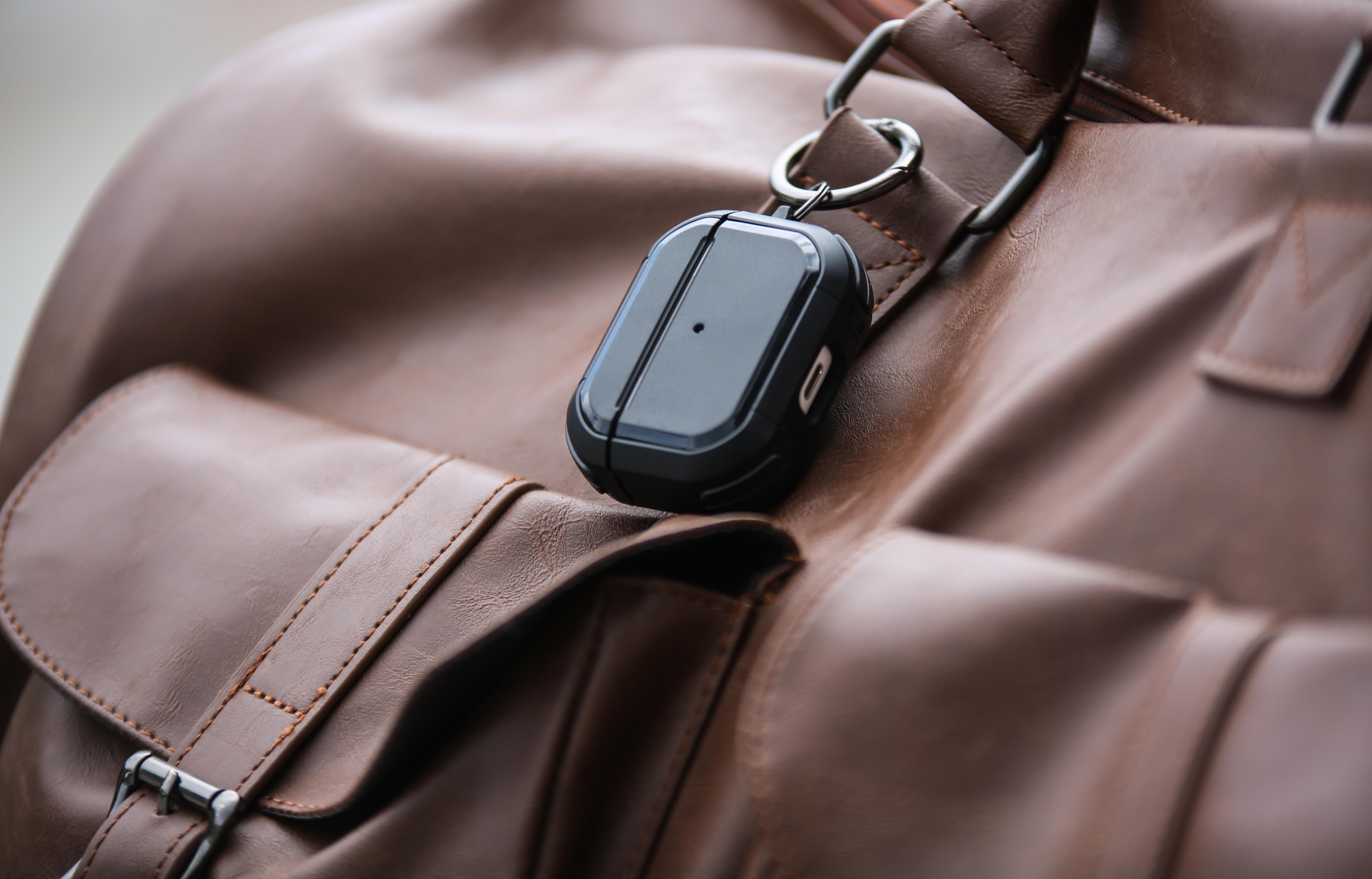 Nahaufnahme einer schwarzen AirPods-Hülle an einer braunen Ledertasche, im Freien.