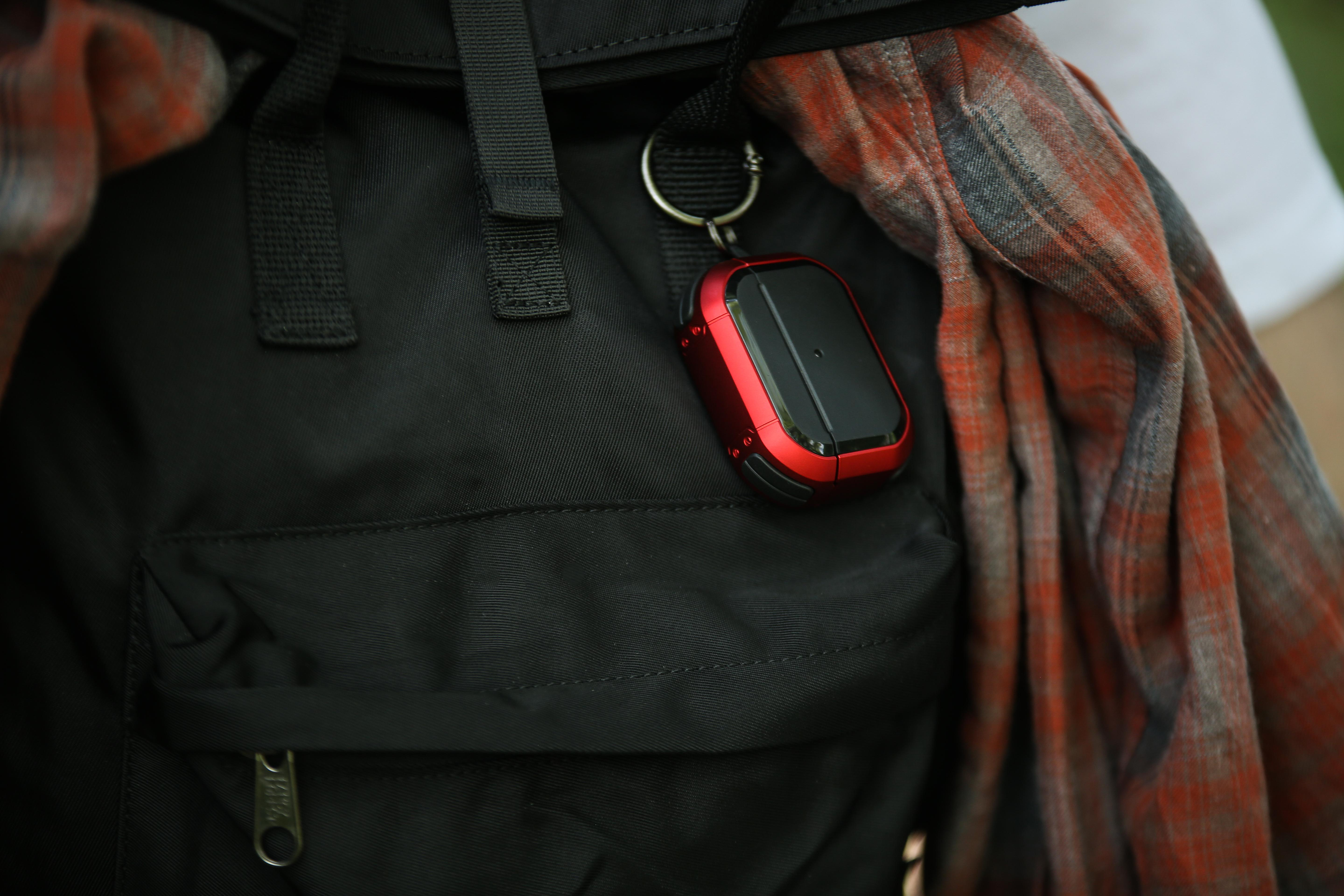 Rotes und schwarzes Ortungsgerät an einem schwarzen Rucksack mit einem rot-schwarz karierten Hemd.