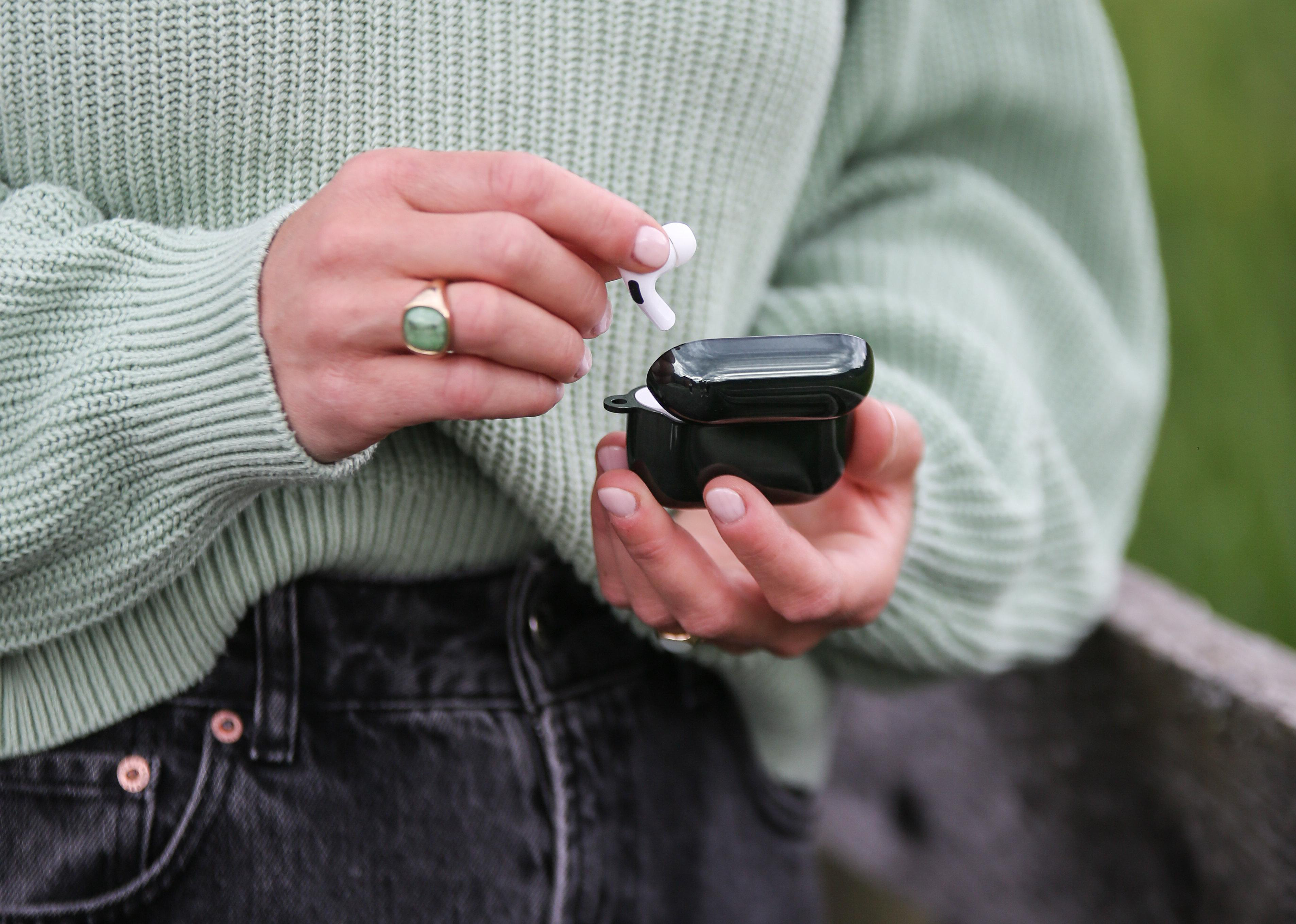 Person hält schwarzes Ladecase mit AirPods, Ring sichtbar.