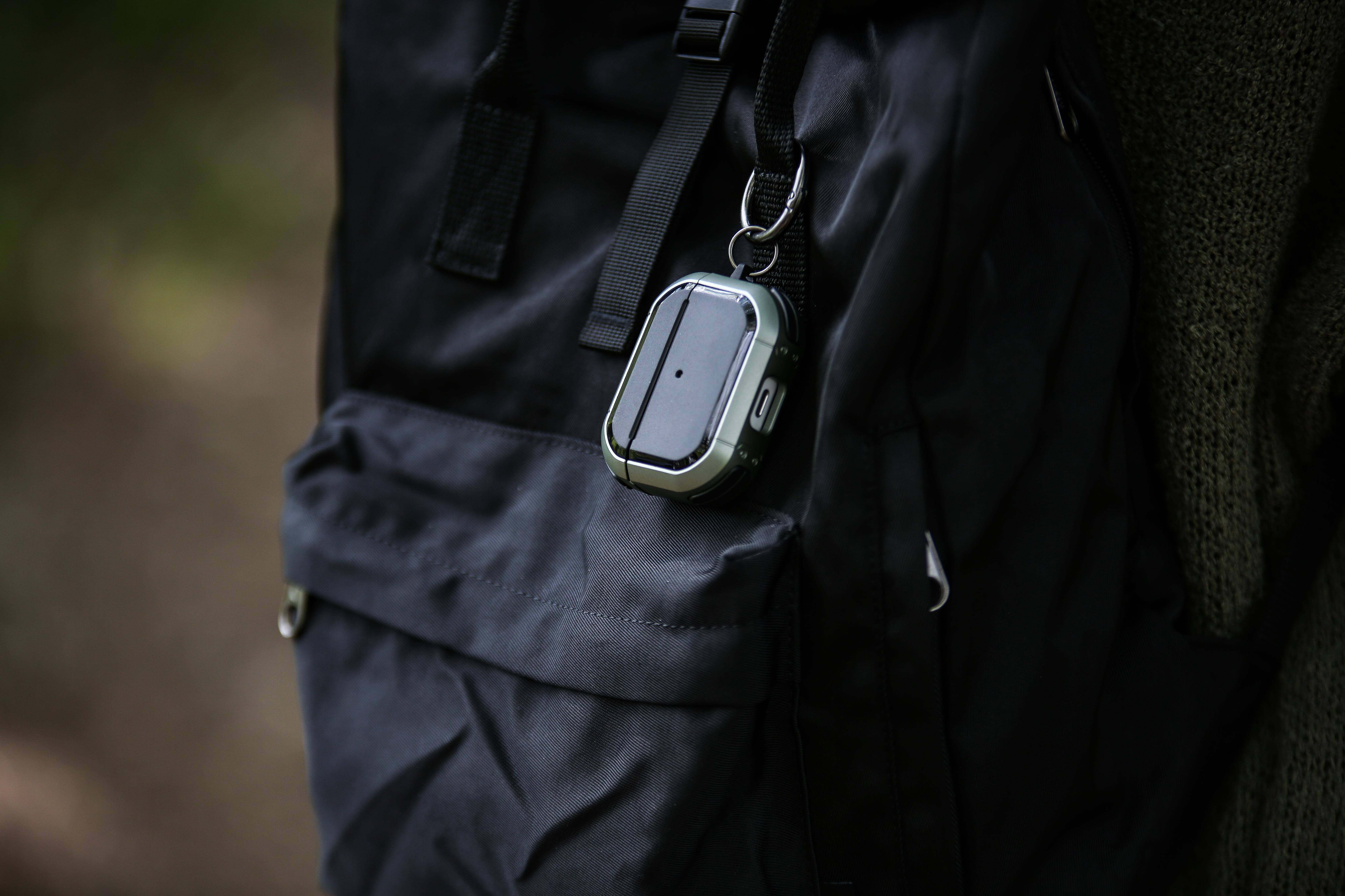 AirPods Pro-Hülle an einem schwarzen Rucksack befestigt. Die Hülle ist grün und schwarz.