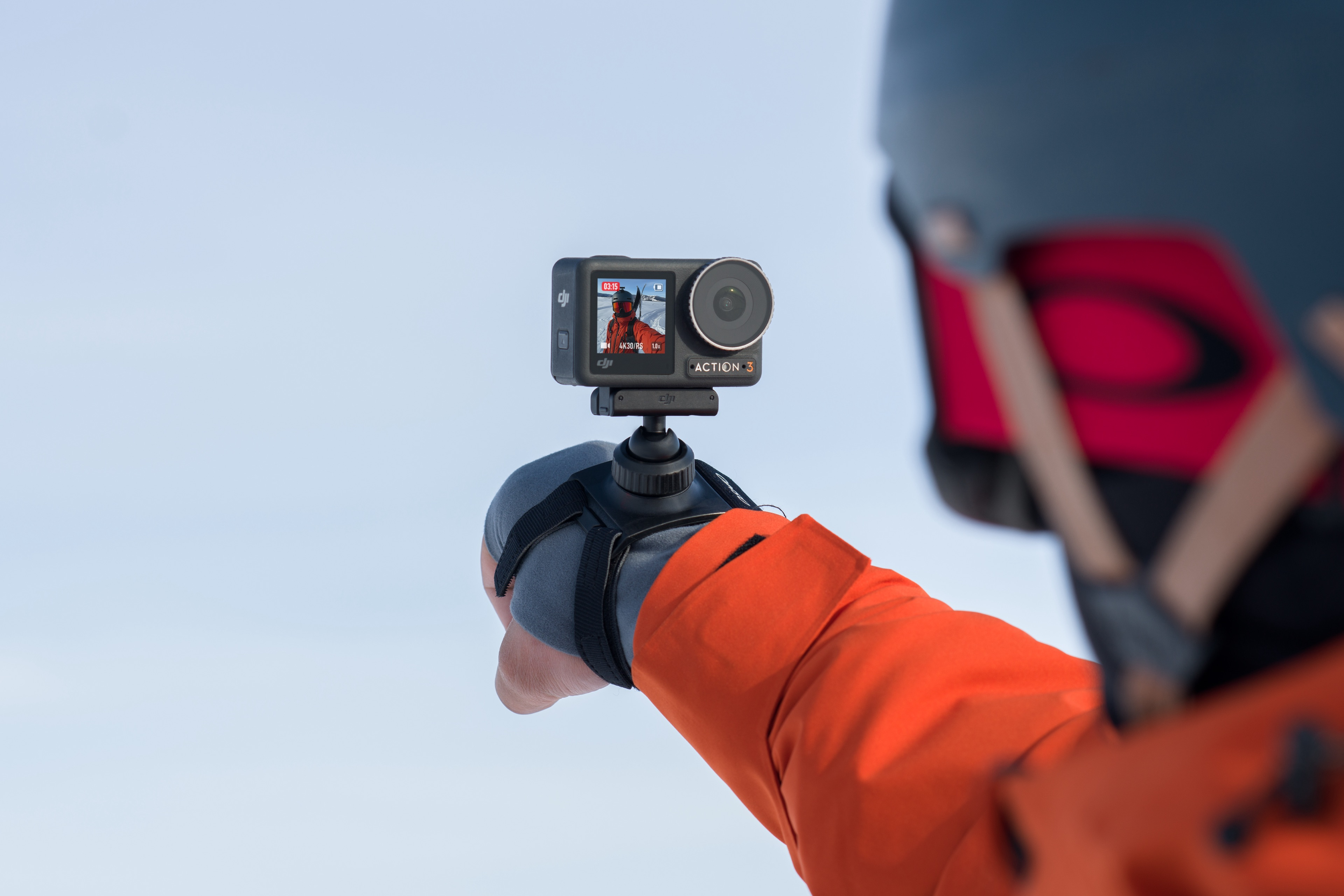 Eine Person hält eine schwarze Action-Kamera in der Hand und trägt einen Skihelm.