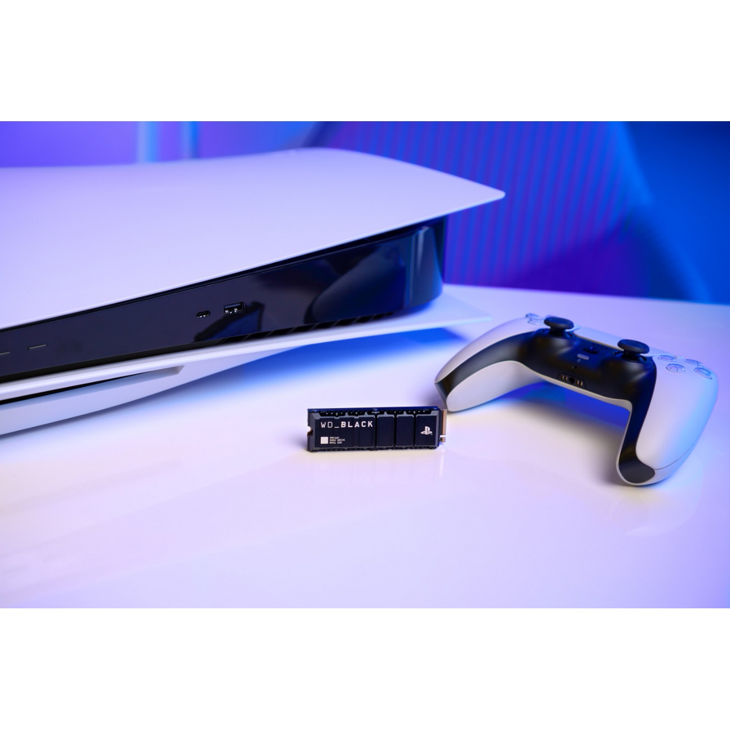 Consola PS5, mando y SSD WD Black sobre superficie blanca con fondo azul.