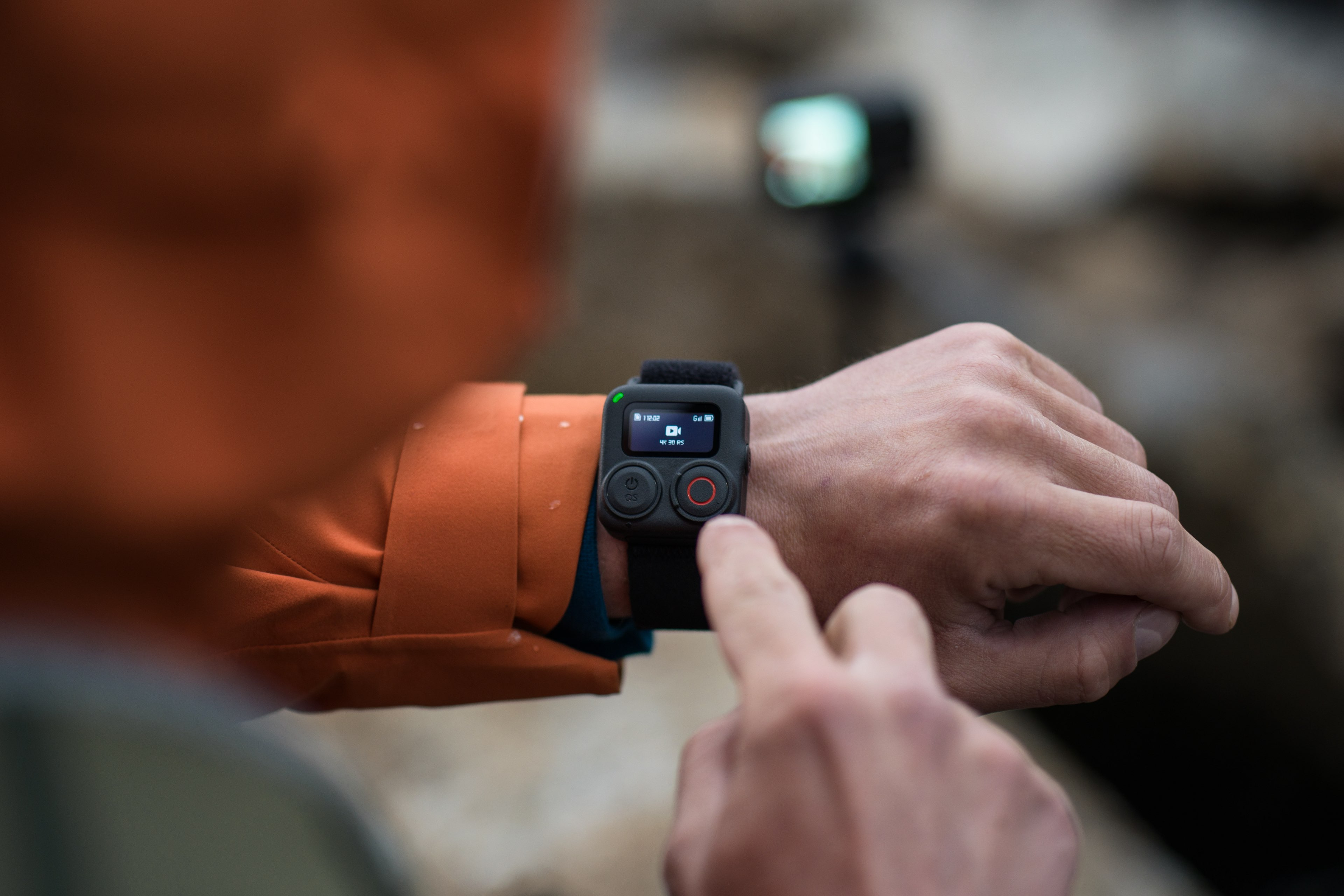 Eine Person mit orangefarbener Jacke benutzt eine Smartwatch mit zwei Knöpfen.