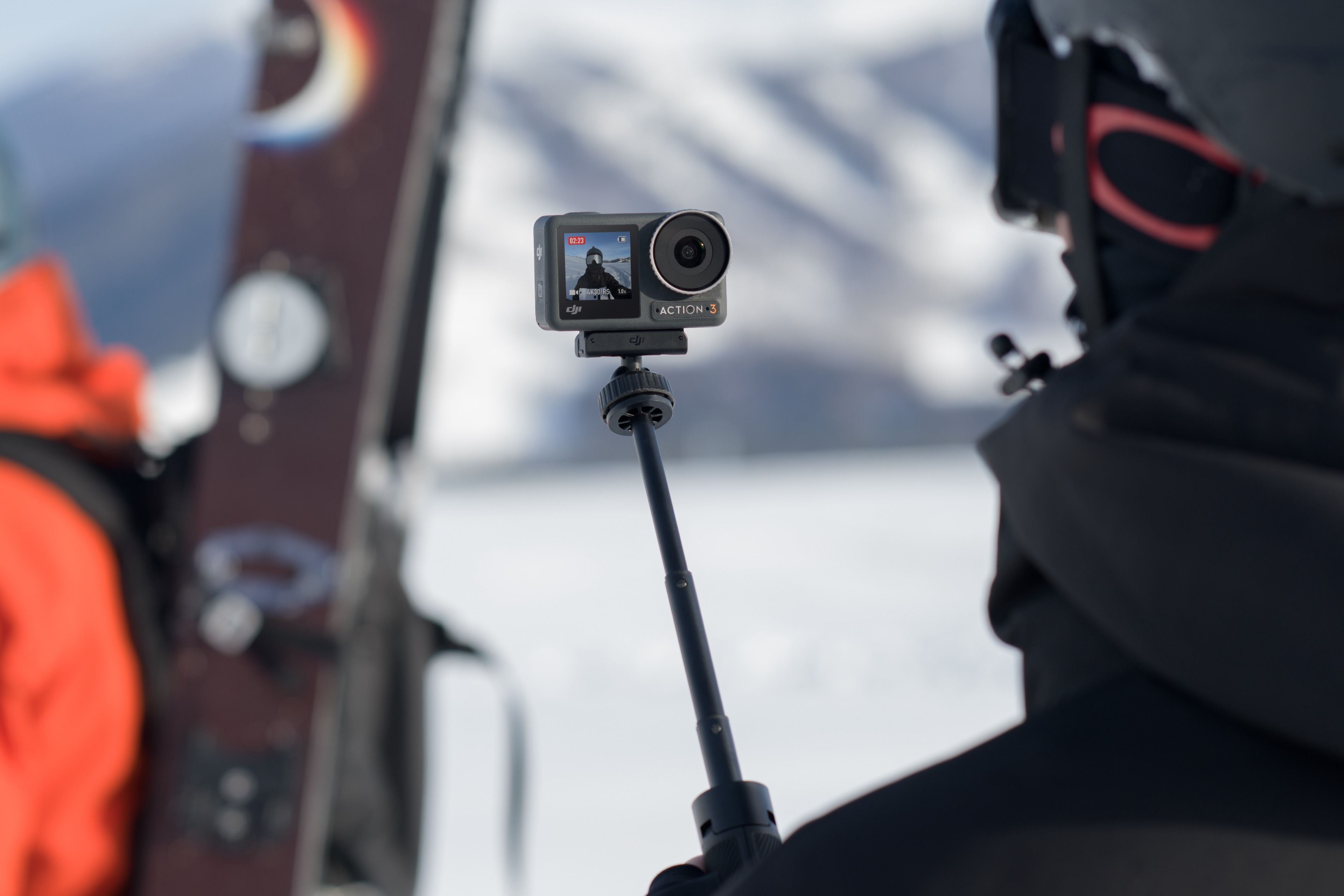 Person nutzt Action-Kamera an Selfie-Stick. Schneebedeckte Berglandschaft auf dem Kamerabildschirm.