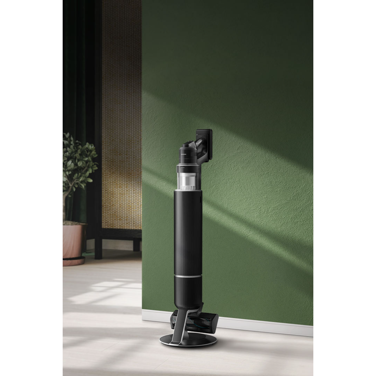 A black and silver cordless vacuum cleaner is mounted on a green wall in front of a wooden floor.