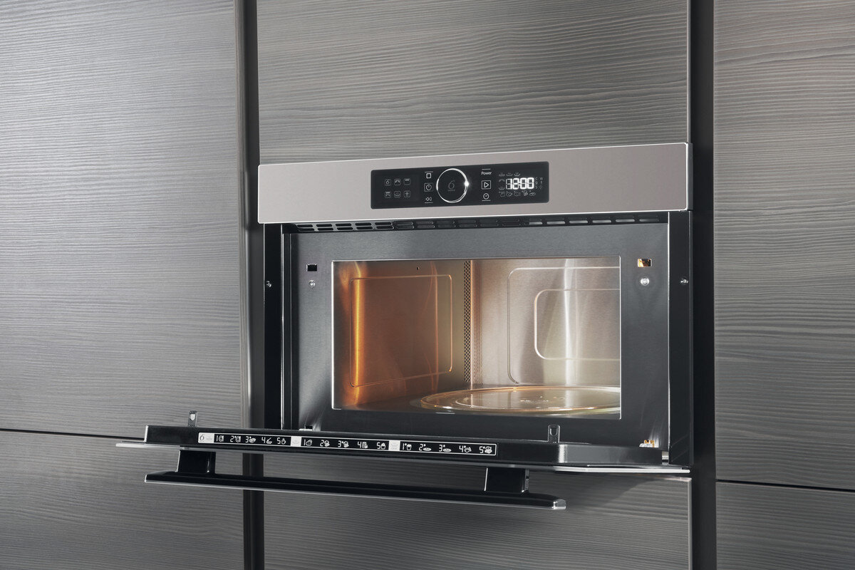 Kuchenka mikrofalowa wbudowana w szafkę. Drzwi są otwarte, widoczne wnętrze. Srebrne wykończenie i szara szafka.