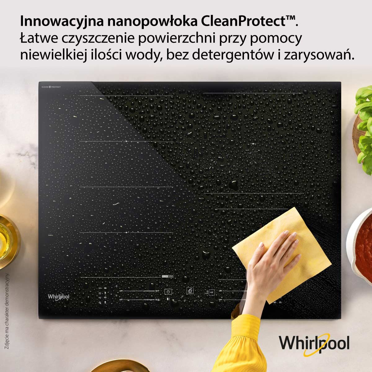 Czarna płyta indukcyjna z kroplami wody i ręką, która ją wyciera.