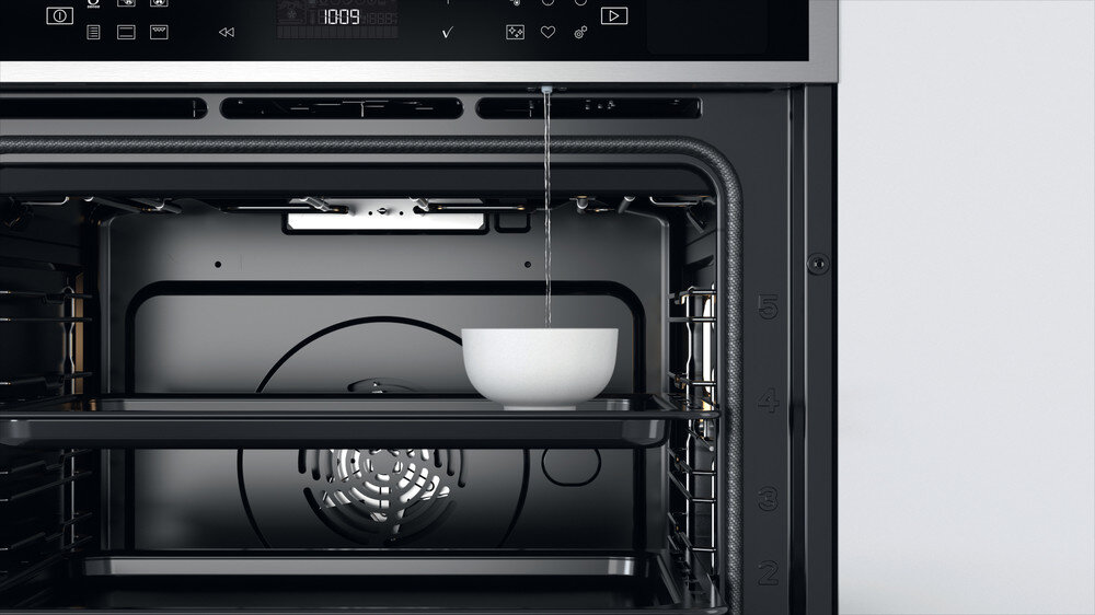 Woda wlewana do białej miski w piekarniku, z otwartymi drzwiami piekarnika.