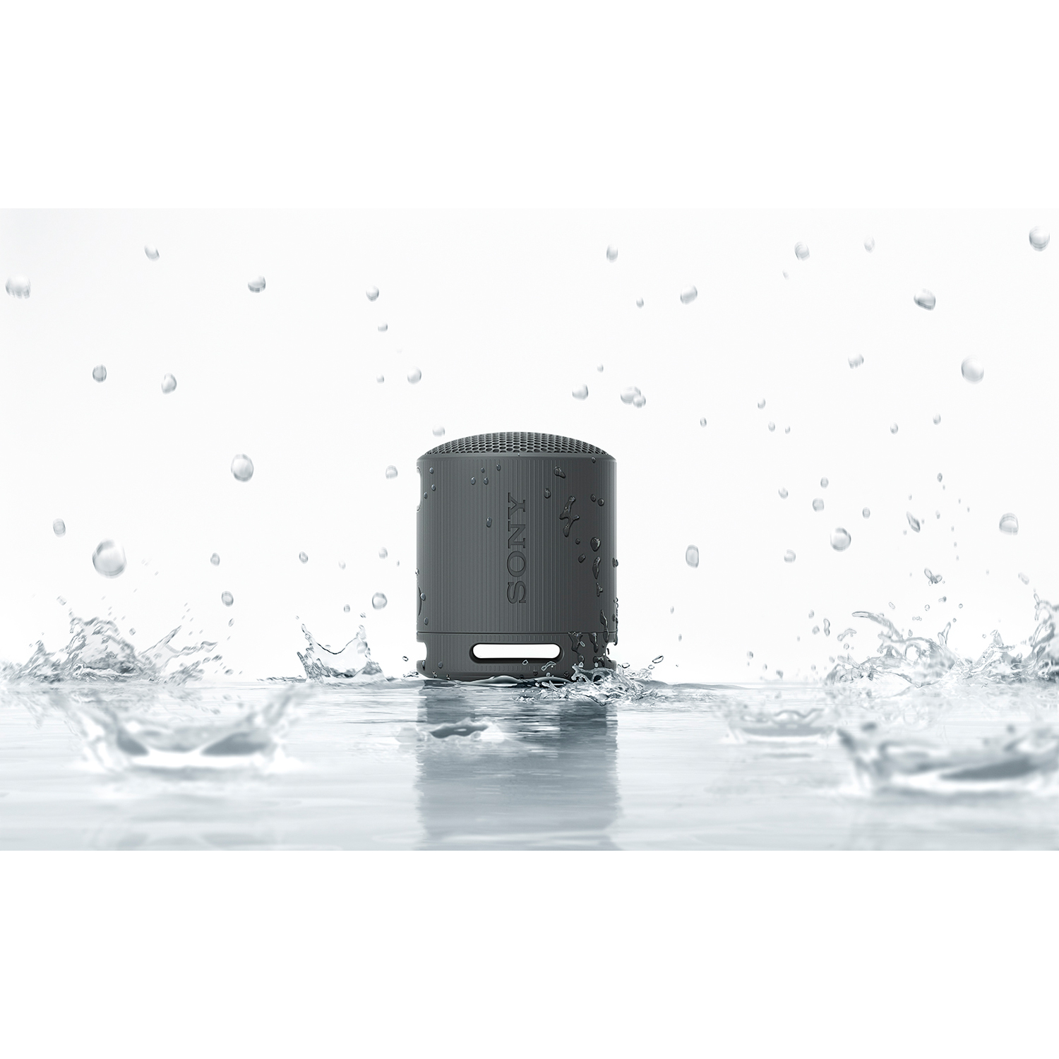 Un altoparlante SONY grigio in acqua con schizzi e gocce intorno.