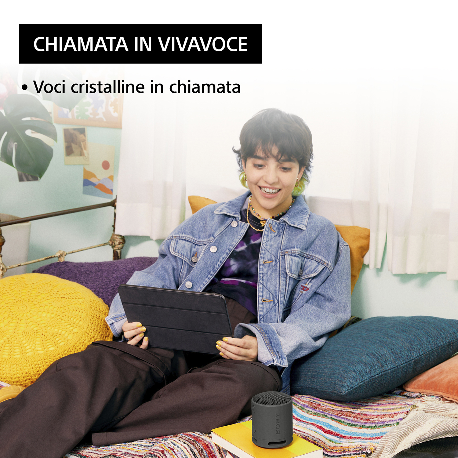 Donna che usa un tablet, piccolo altoparlante sulla scrivania. Testo: 'Chiamata in vivavoce'. Stanza colorata.