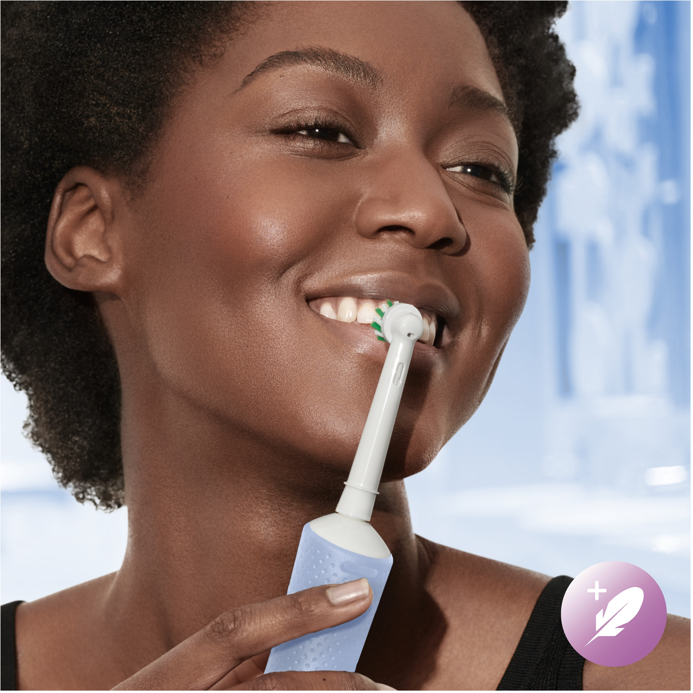 Donna che si lava i denti con uno spazzolino elettrico. Un'icona di piuma è visibile.