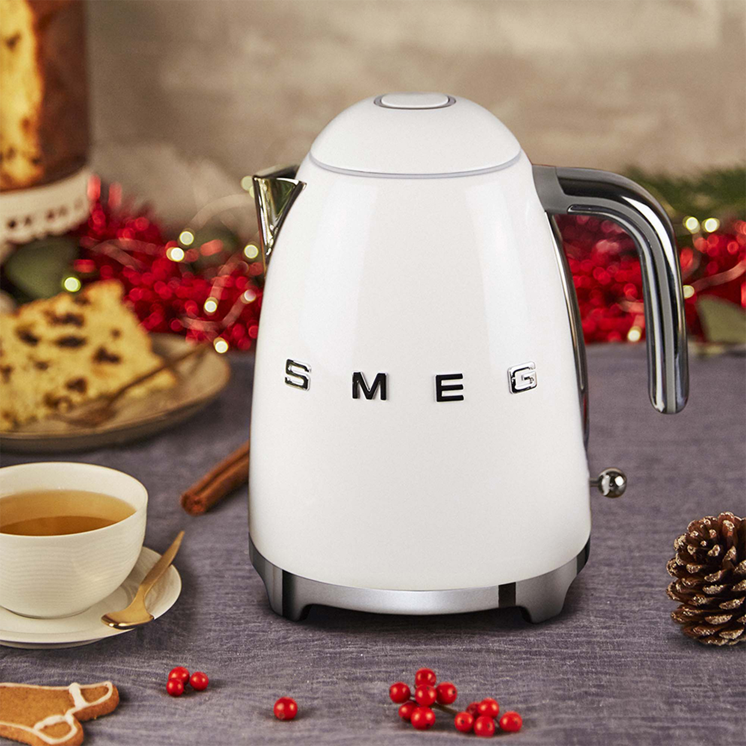 Un bollitore SMEG bianco su un tavolo con decorazioni natalizie. Altri oggetti includono cibo e ornamenti.