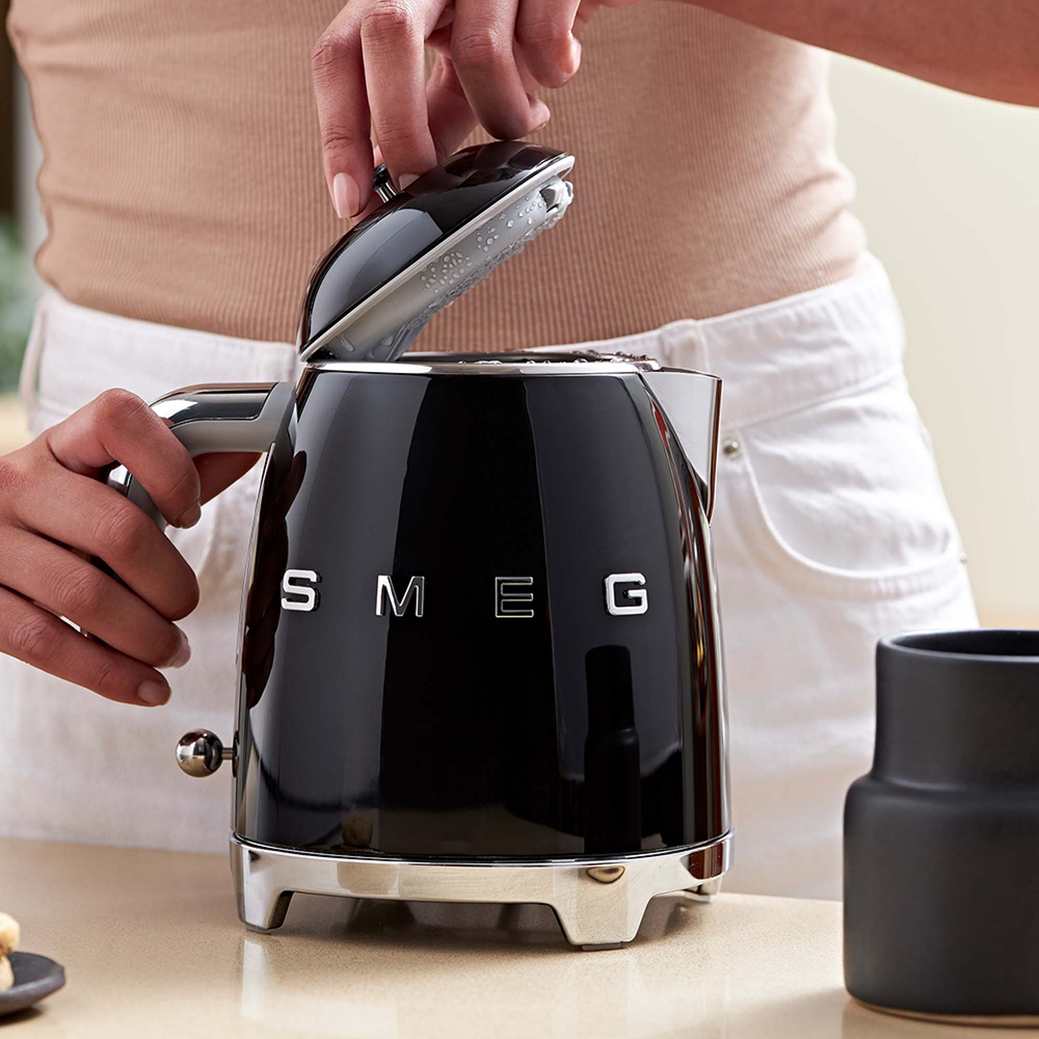 Persona che apre il coperchio di un bollitore SMEG nero.