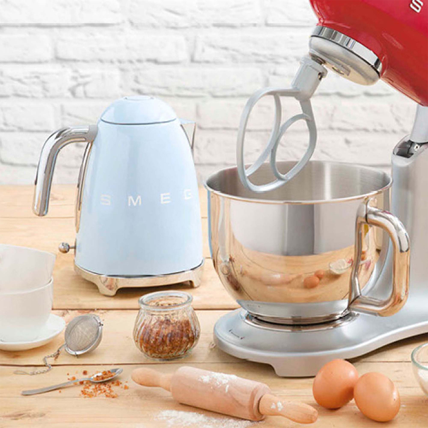 Scena di cucina con un bollitore Smeg azzurro e un mixer a supporto argentato. Tavolo di legno.