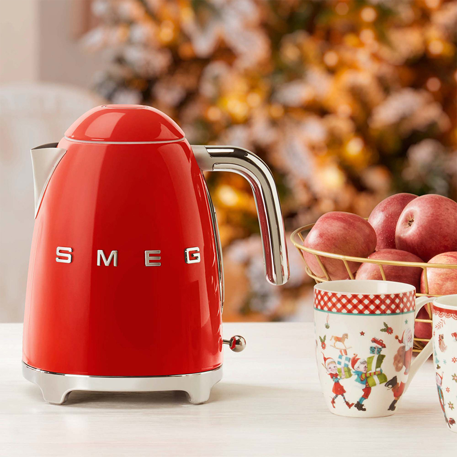 Bollitore SMEG rosso sul tavolo. Mele, tazze e sfondo sfocato con luci.