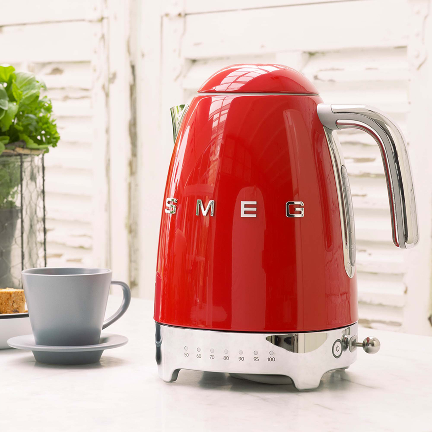 Bollitore SMEG rosso su una superficie bianca. Accanto c'è una tazza e un piattino grigi.
