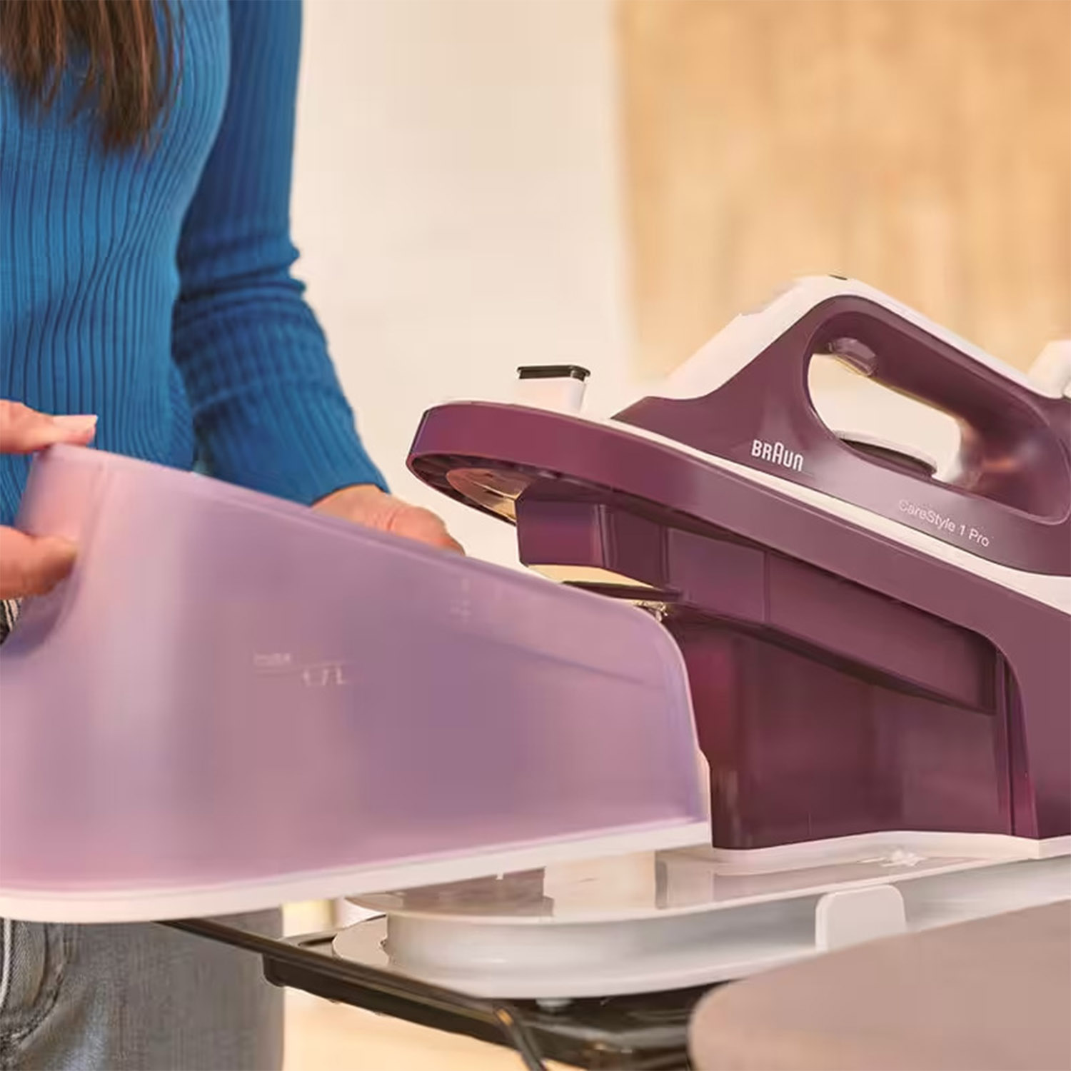 Donna che riempie il serbatoio dell'acqua di un ferro da stiro viola. Il ferro è bianco e viola, su una superficie bianca.