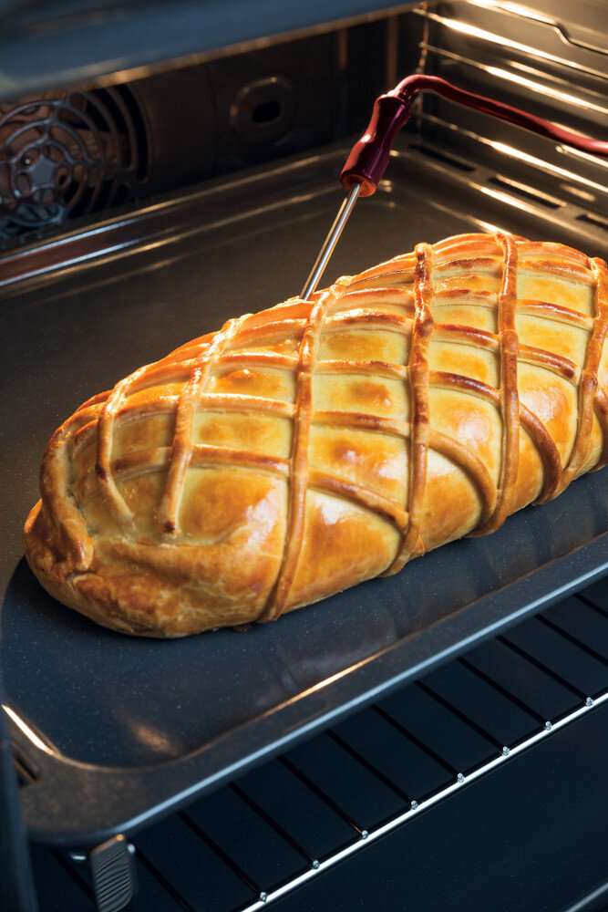 Złotobrązowy beef wellington w piekarniku, z włożonym termometrem.
