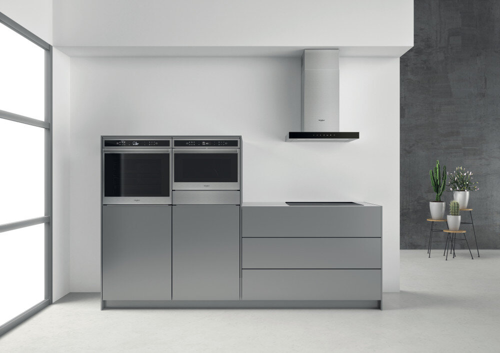 Nowoczesna kuchnia z dwoma piekarnikami, płytą grzejną i okapem. Szare szafki i białe ściany.