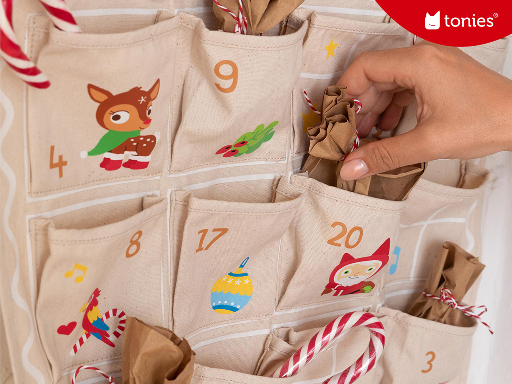 Adventskalender mit nummerierten Taschen. Eine Hand greift in eine Tasche, um ein Geschenk zu holen.