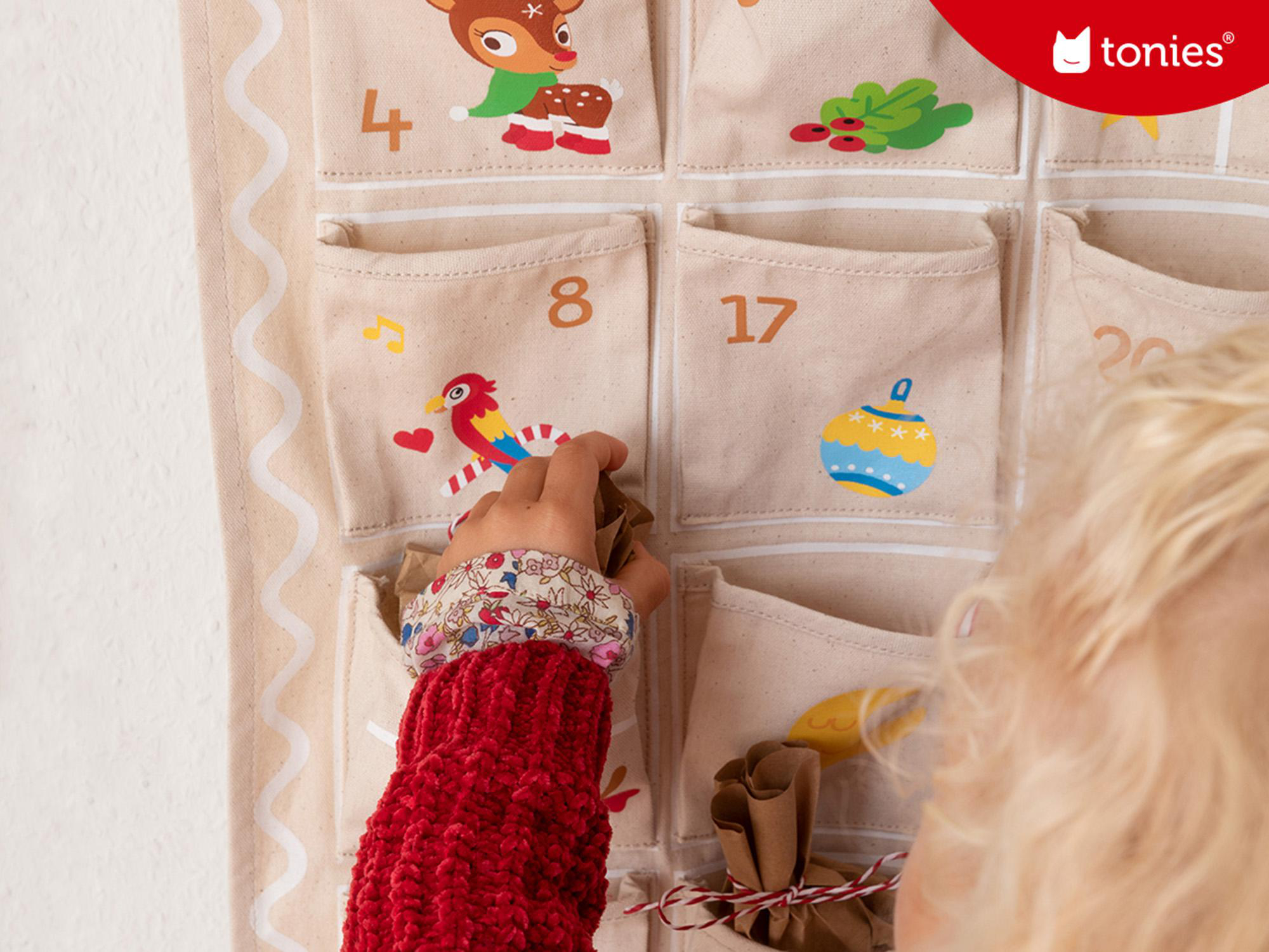 Ein Kinderhand, die in einen Adventskalender greift, mit nummerierten Taschen und Illustrationen.