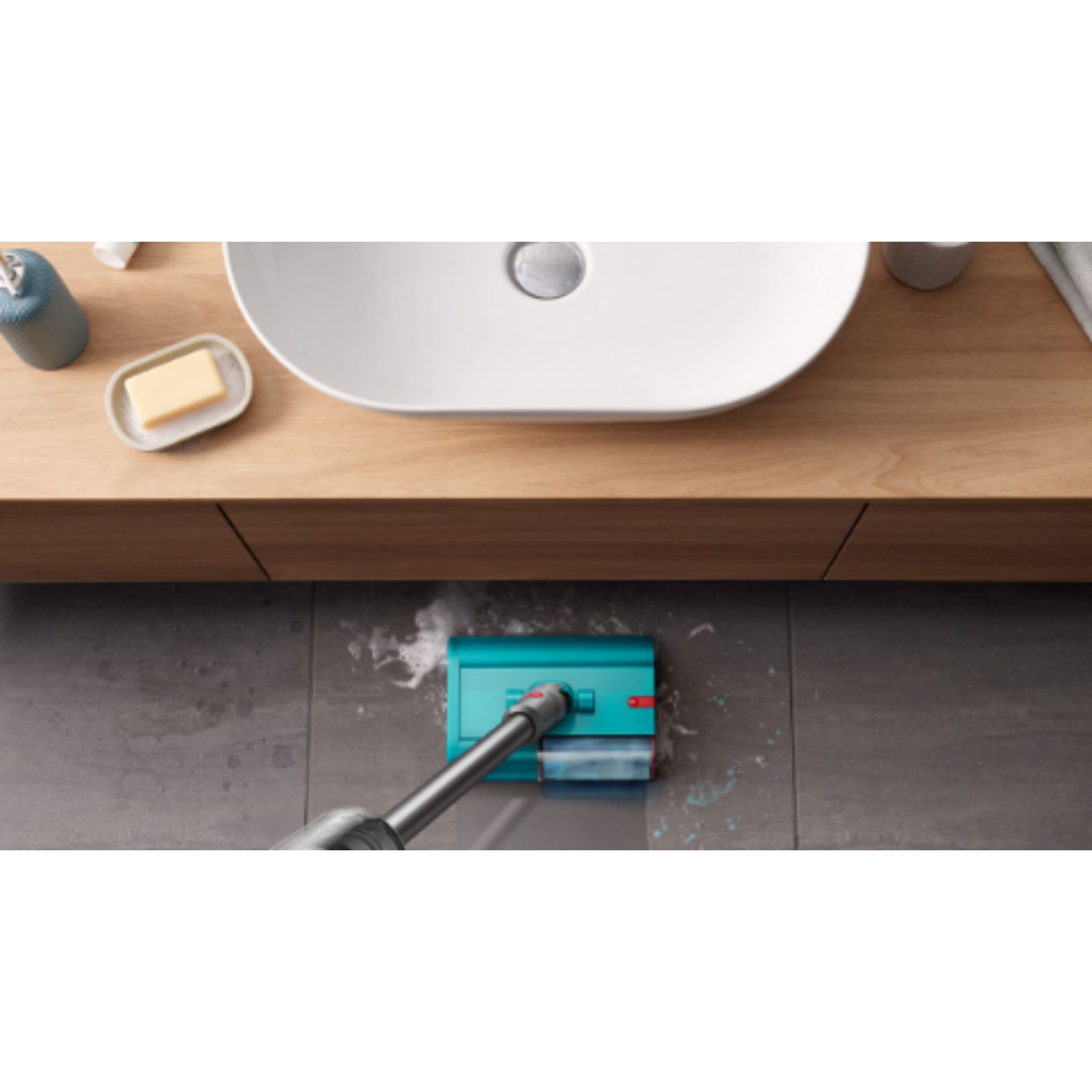 A blue and gray vacuum cleaner is cleaning a gray tile floor in a bathroom.